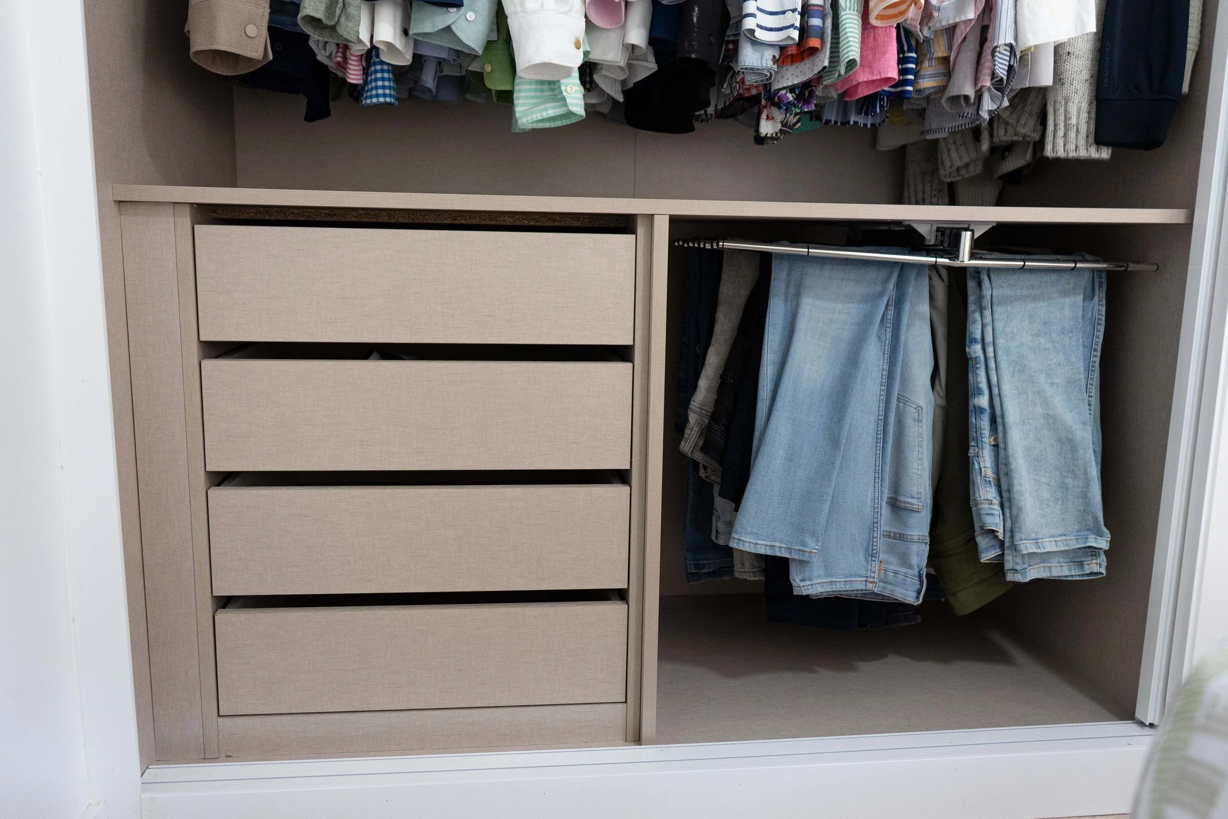 Armario de ropa con prendas colgadas y cajones cerrados en tonos beige.