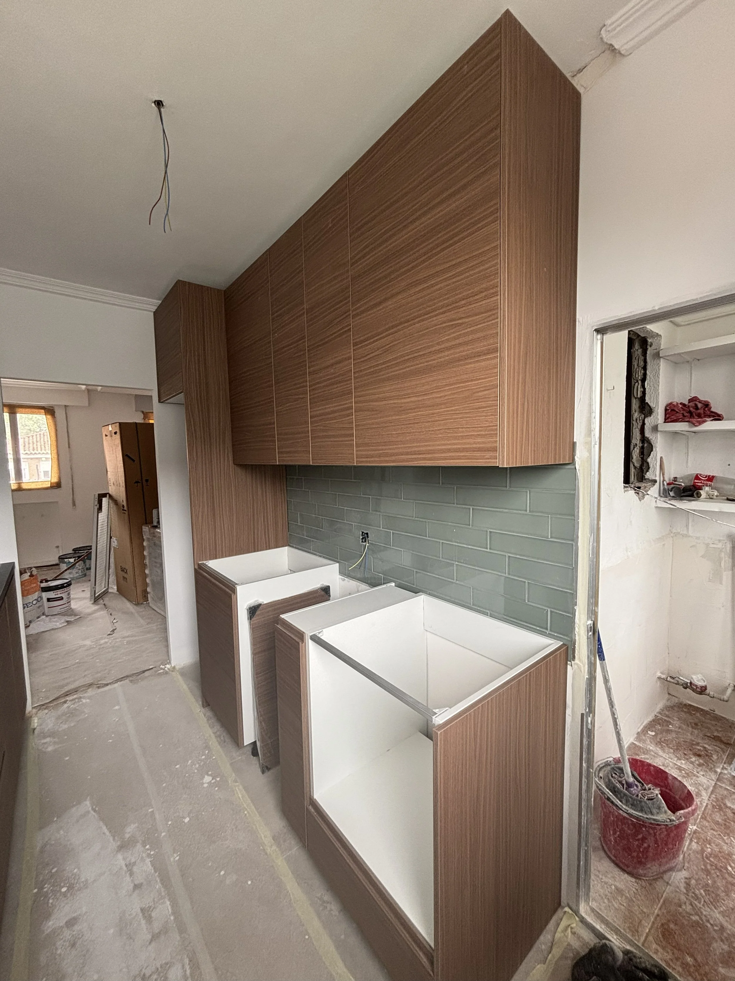 Cocina en construcción con gabinetes de madera, baldas, pared de baldosas y áreas para electrodomésticos instalados.