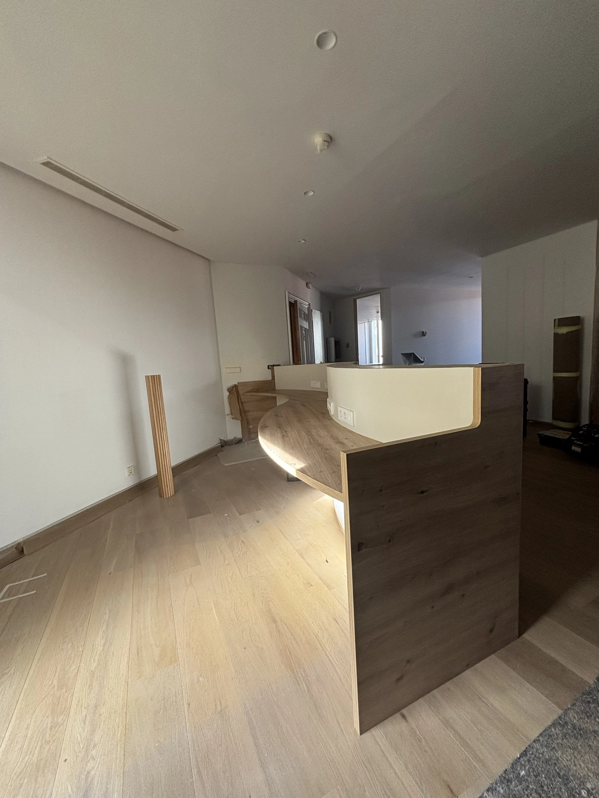 Interior de oficina en construcción con mueble de madera y cables en el suelo.