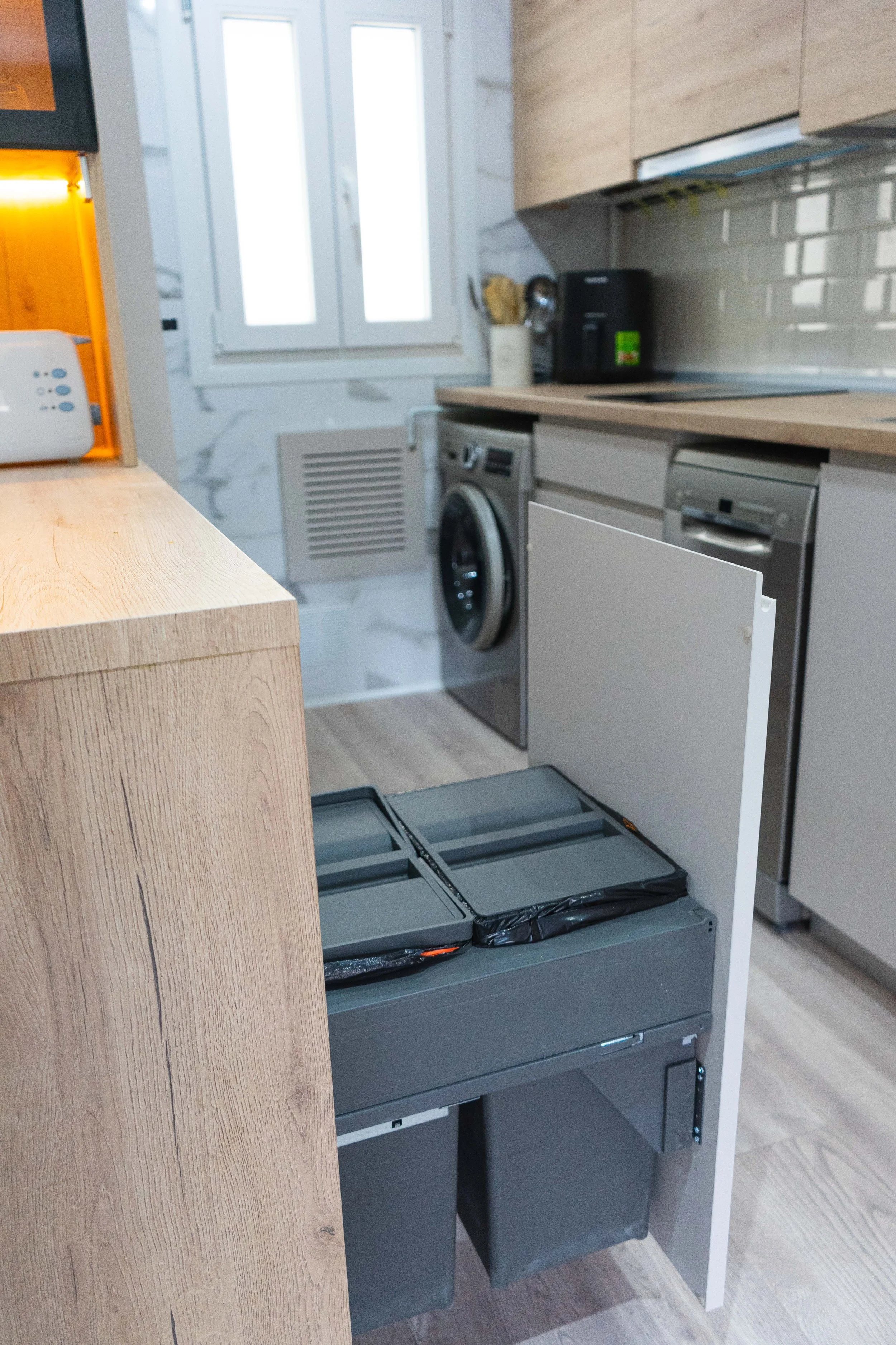 Cajón de basura en una cocina moderna con electrodomésticos y muebles de madera.