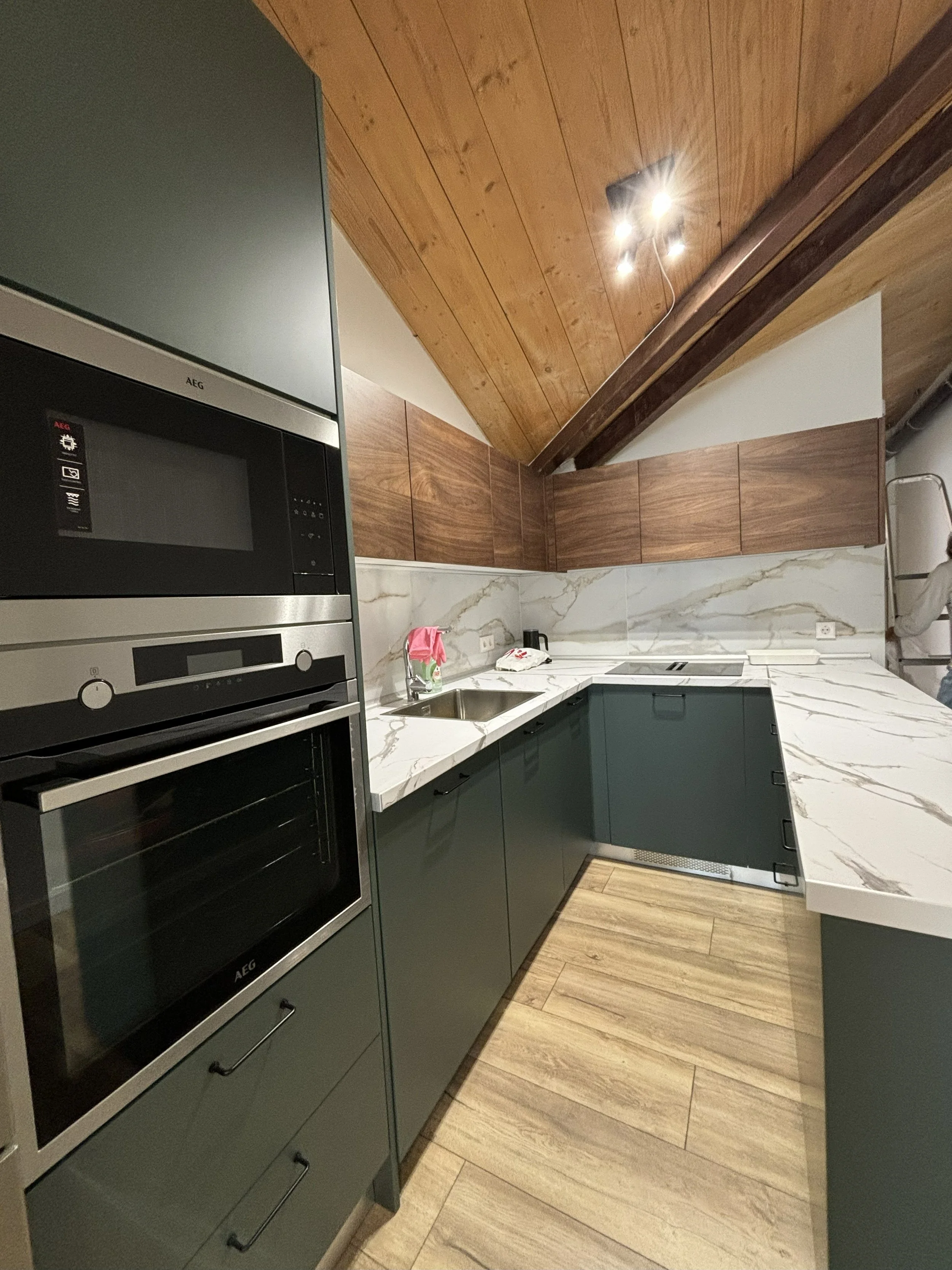 Cocina moderna con armarios oscuros, encimera de mármol, techos de madera y electrodomésticos de acero inoxidable.