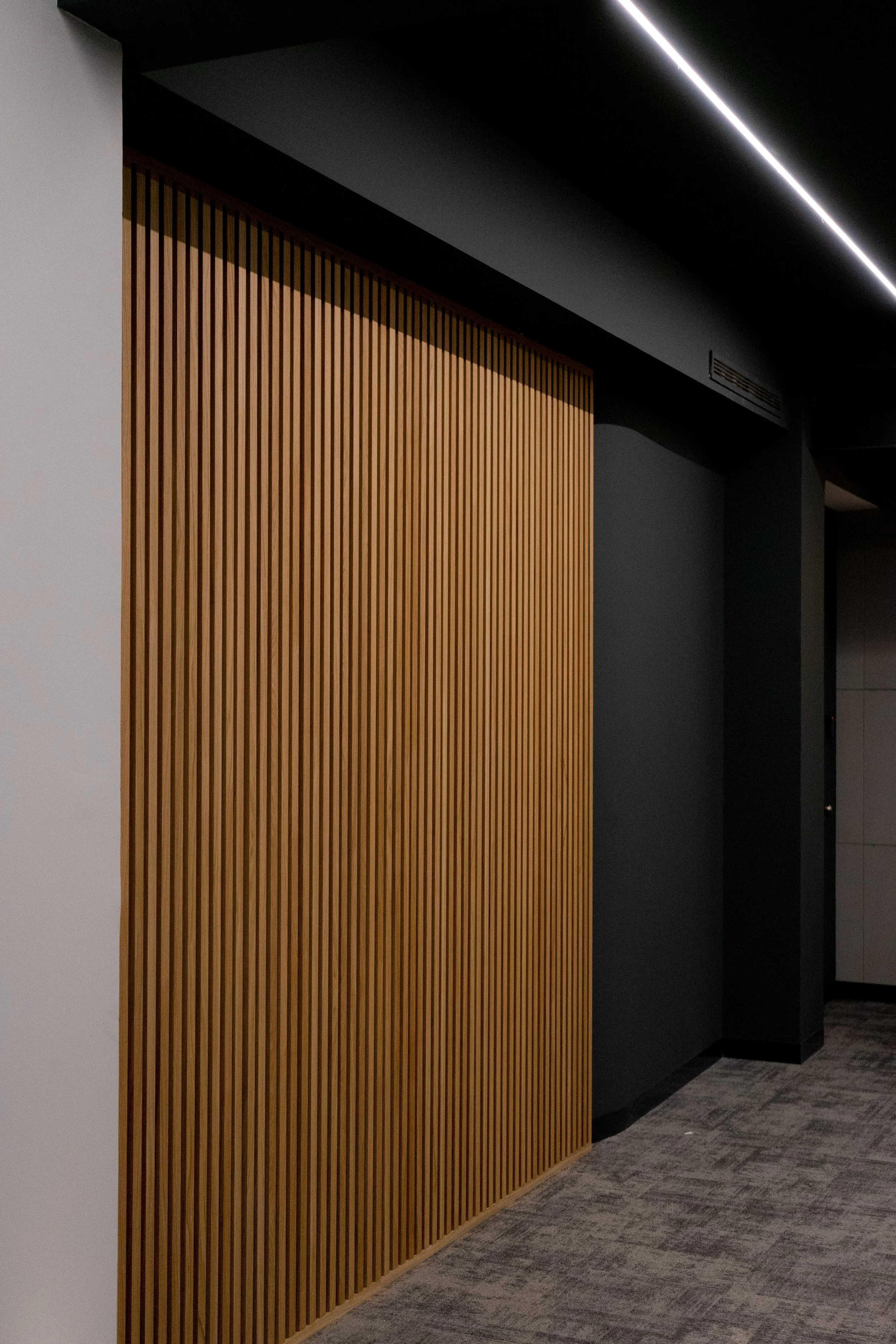 Pared interior con panel de madera listrada y techo negro con iluminación LED.