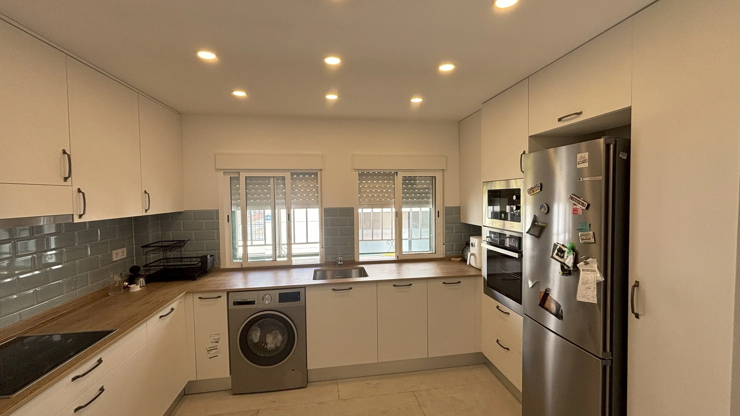 Cocina moderna con gabinetes blancos, electrodomésticos de acero inoxidable y ventanas grandes.