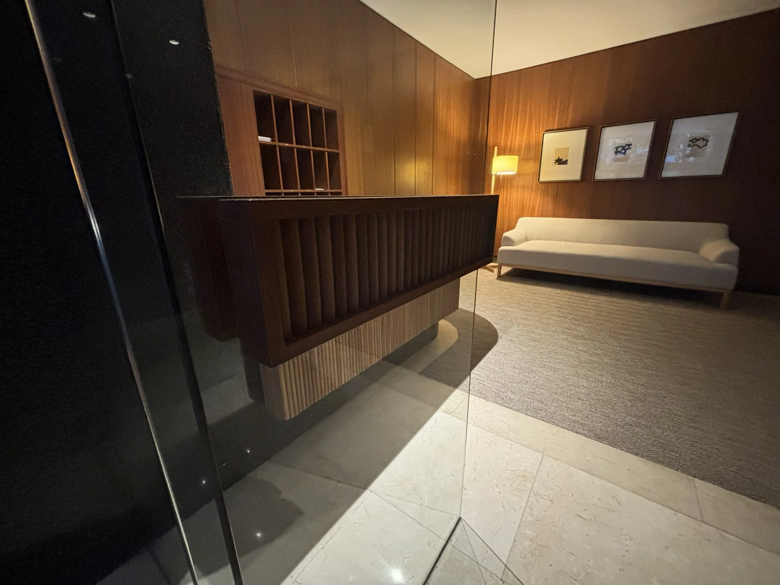 Sala de estar con paredes de madera, sillón blanco, lámpara de pie con pantalla amarilla, cuadros en la pared y alfombra beige