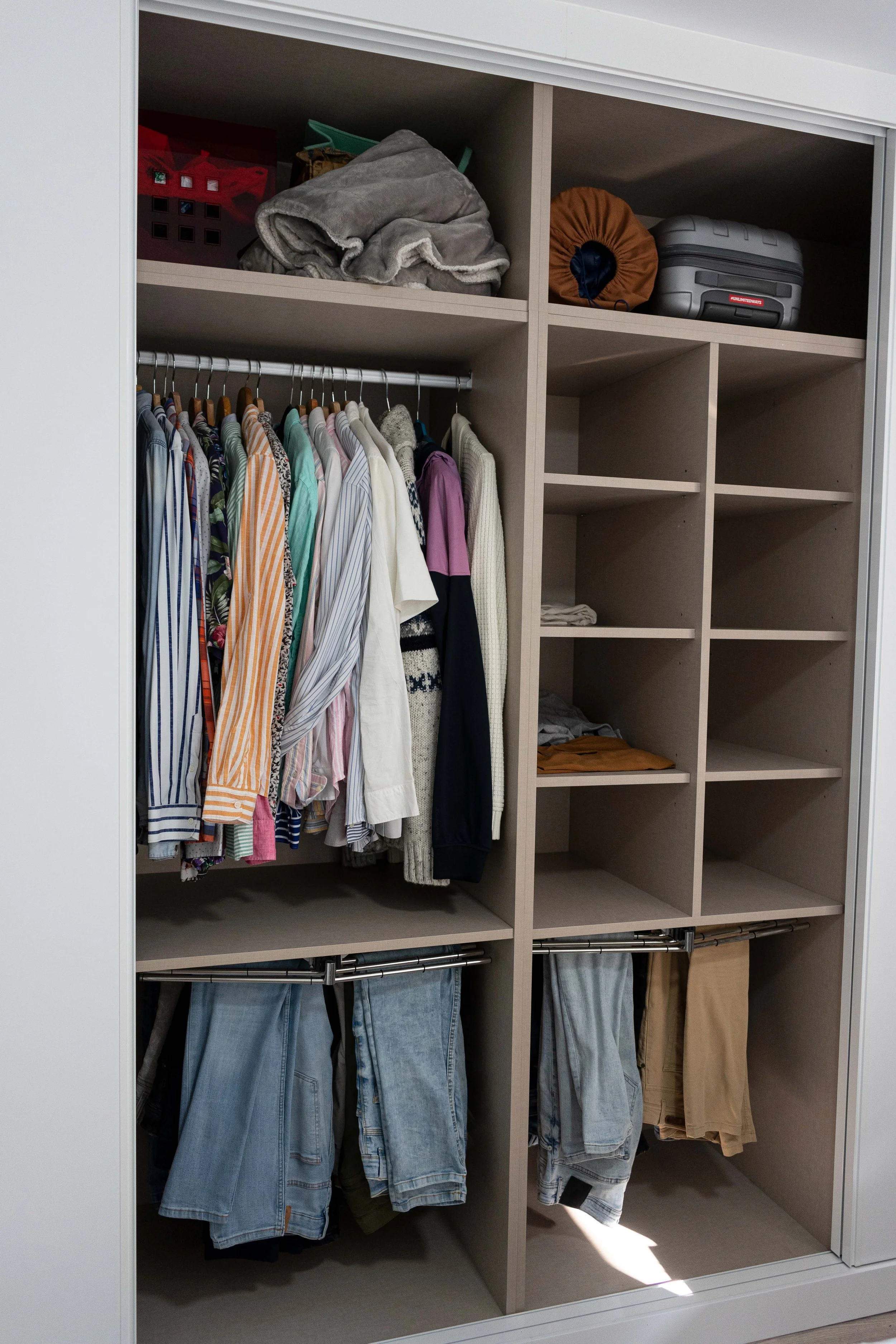 Armario con ropa colgada, ropa doblada en estantes y objetos diversos en las repisas.