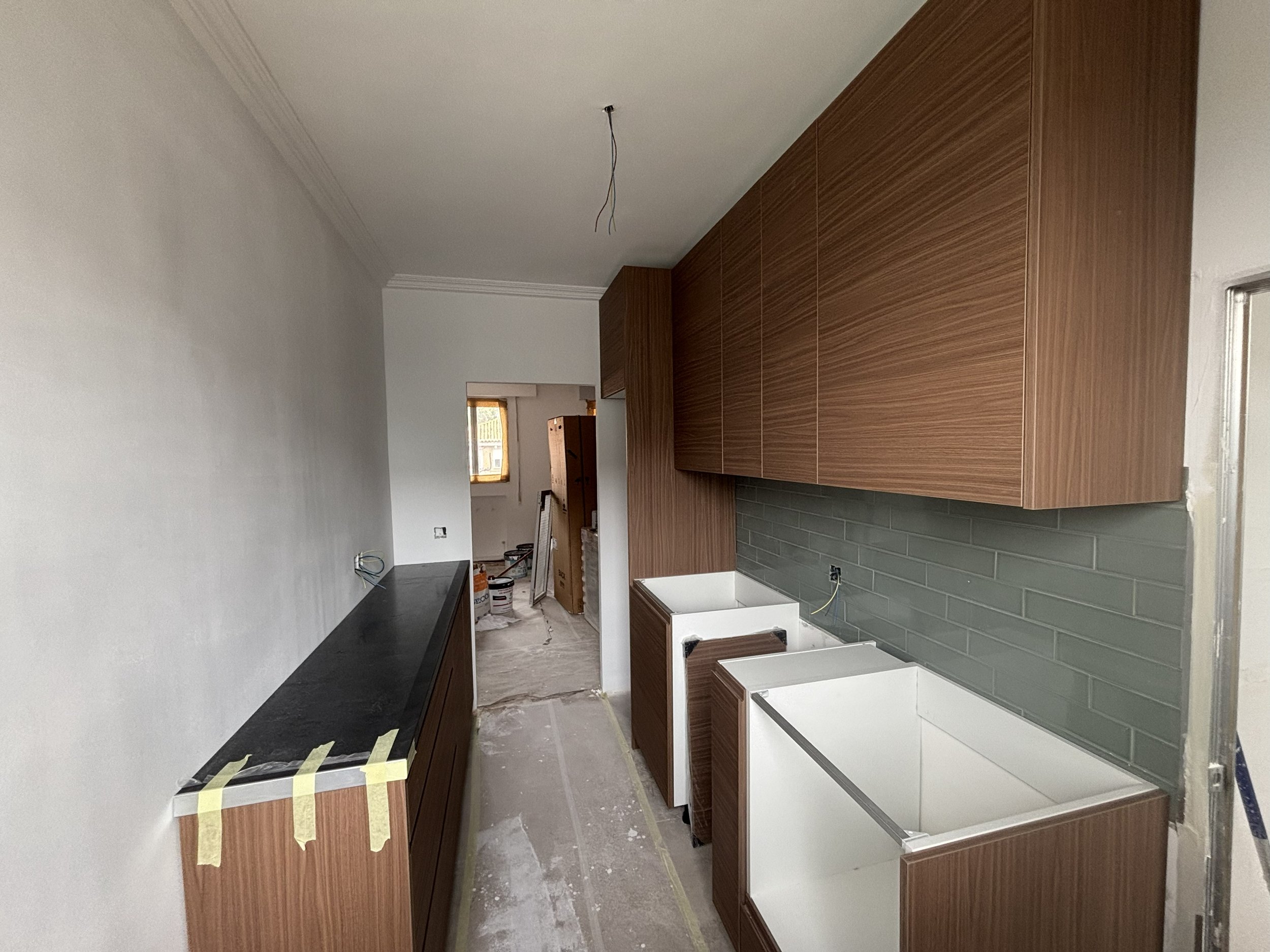 Cocina en construcción con gabinetes de madera, paredes de azulejos grises, y espacios sin electrodomésticos instalados.