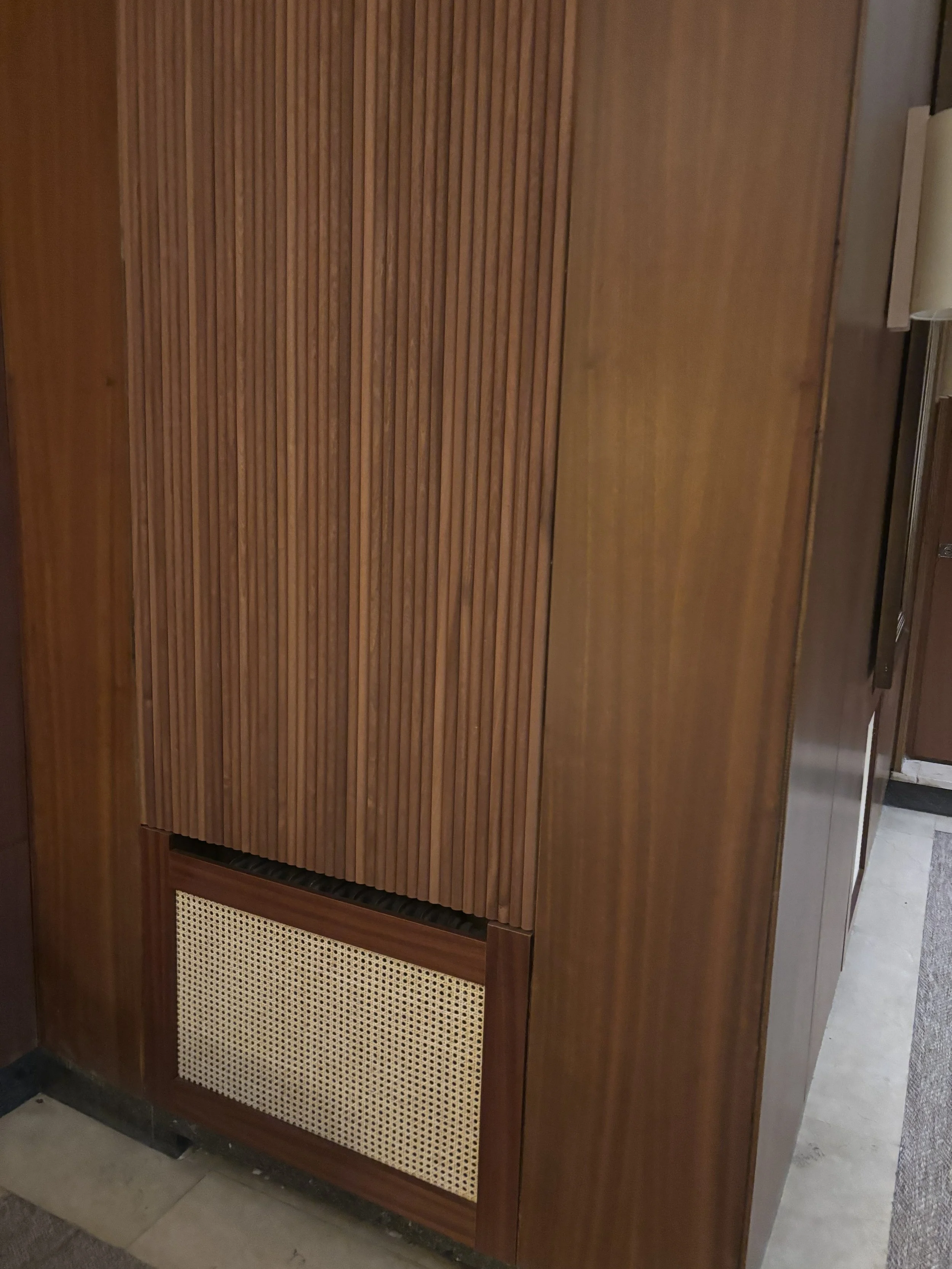 Un mueble de madera con puertas con tiras verticales y una rejilla en la parte inferior derecha.