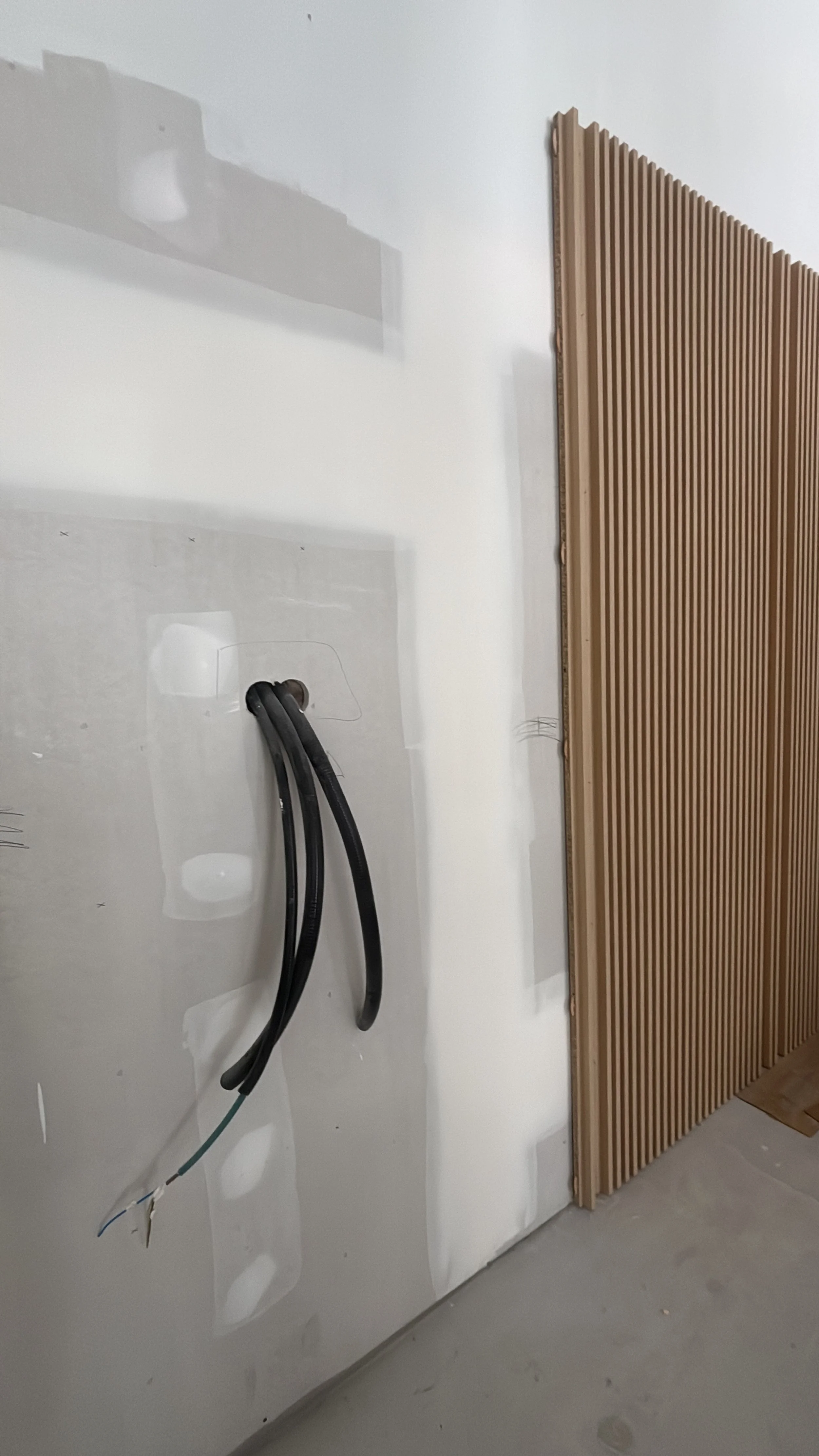 Pared blanca con cables eléctricos colgados y panel de madera en construcción.