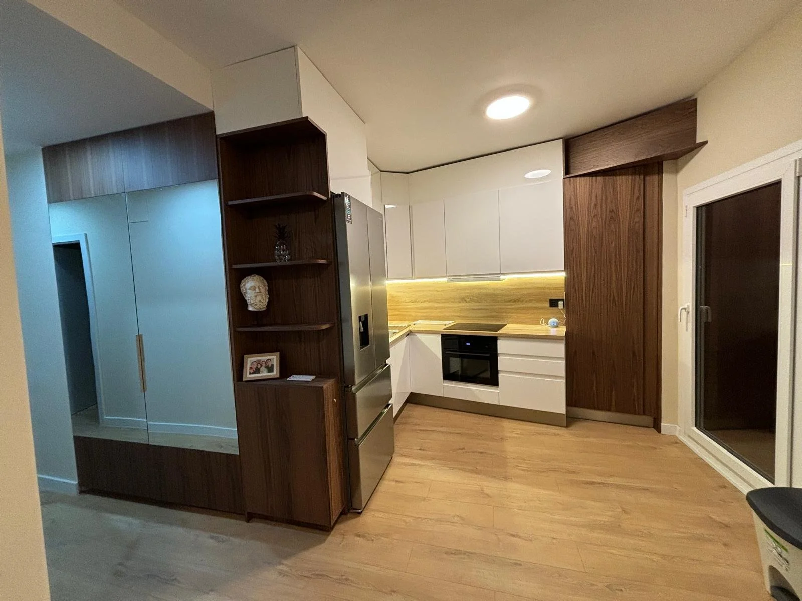 Cocina moderna con gabinetes blancos y madera, electrodomésticos de acero inoxidable y una puerta de vidrio corrediza.