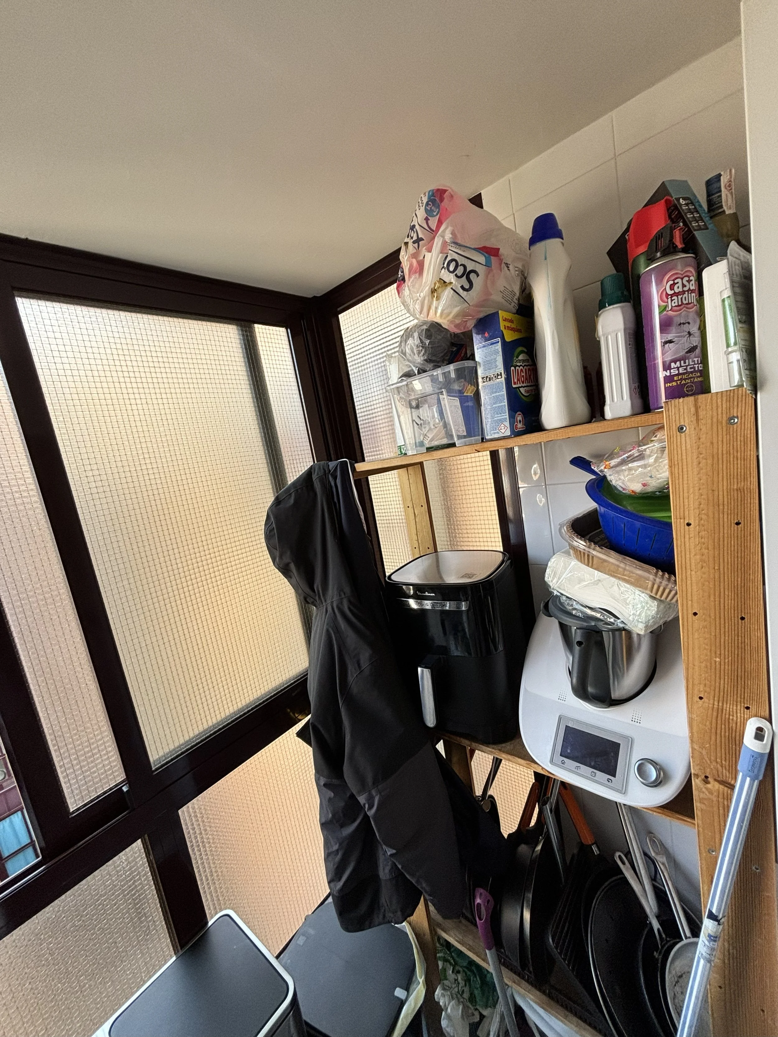 Estantería de madera con productos de limpieza, utensilios de cocina, y ropa en un espacio de cocina o lavandería.