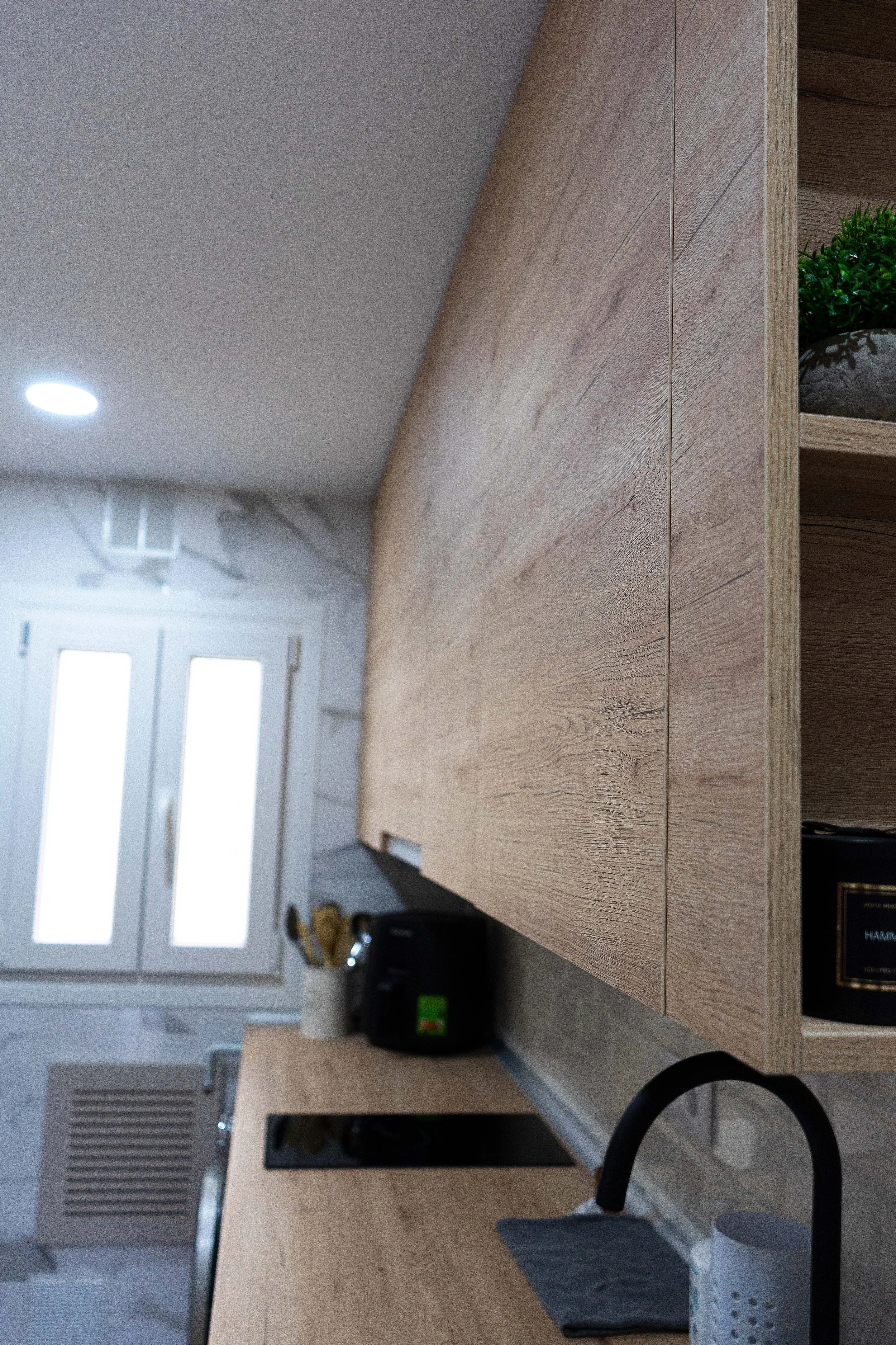 Vista de una cocina moderna con gabinetes de madera, una ventana, una estufa y una mesa de madera.