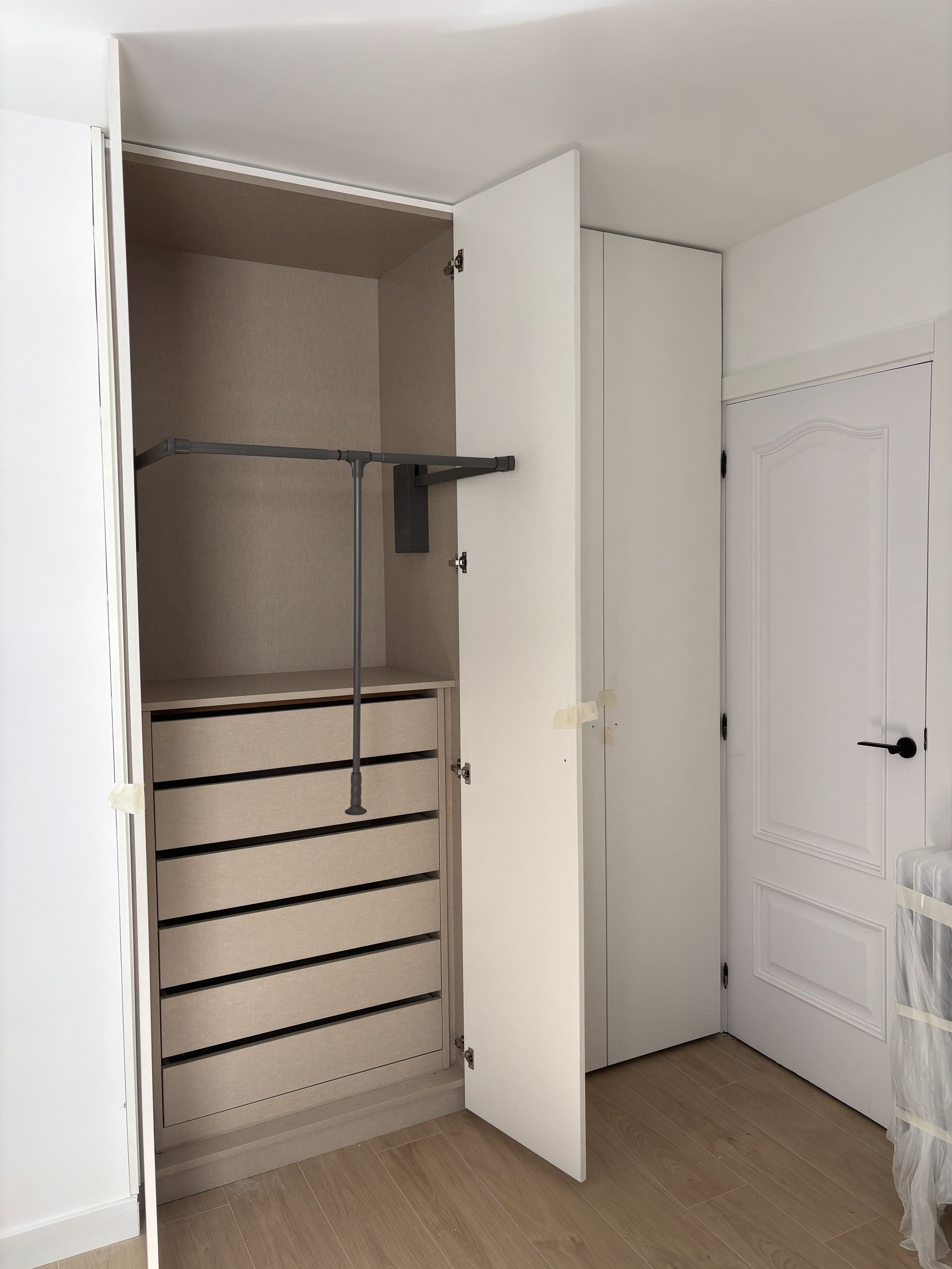 Closet abierto con gavetas, barra para colgar ropa y un espacio vacío  en una habitación con suelo de madera.