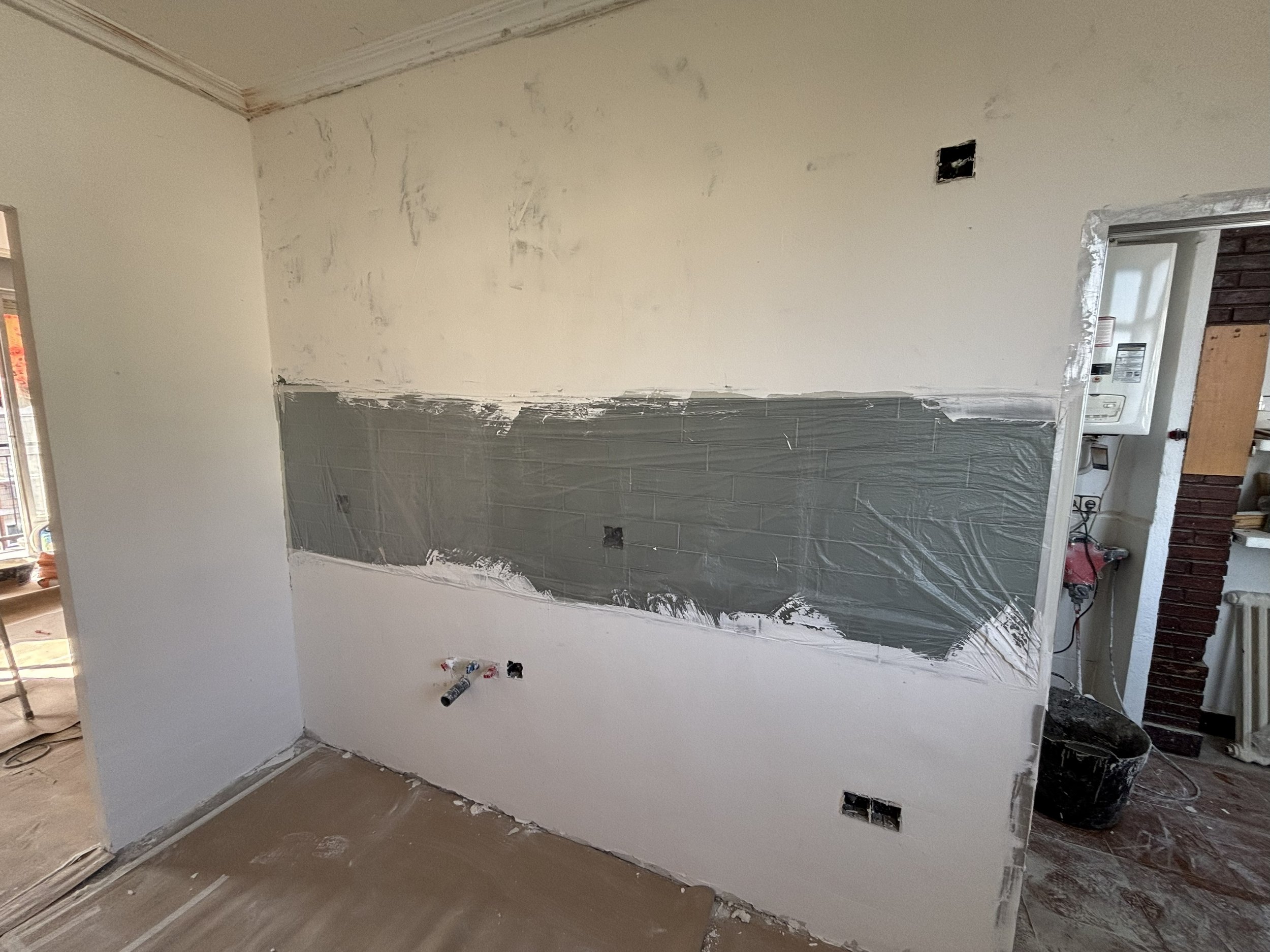 Pared de una habitación en proceso de renovar, con pintura y tiles en progreso, herramientas y cableado visible.