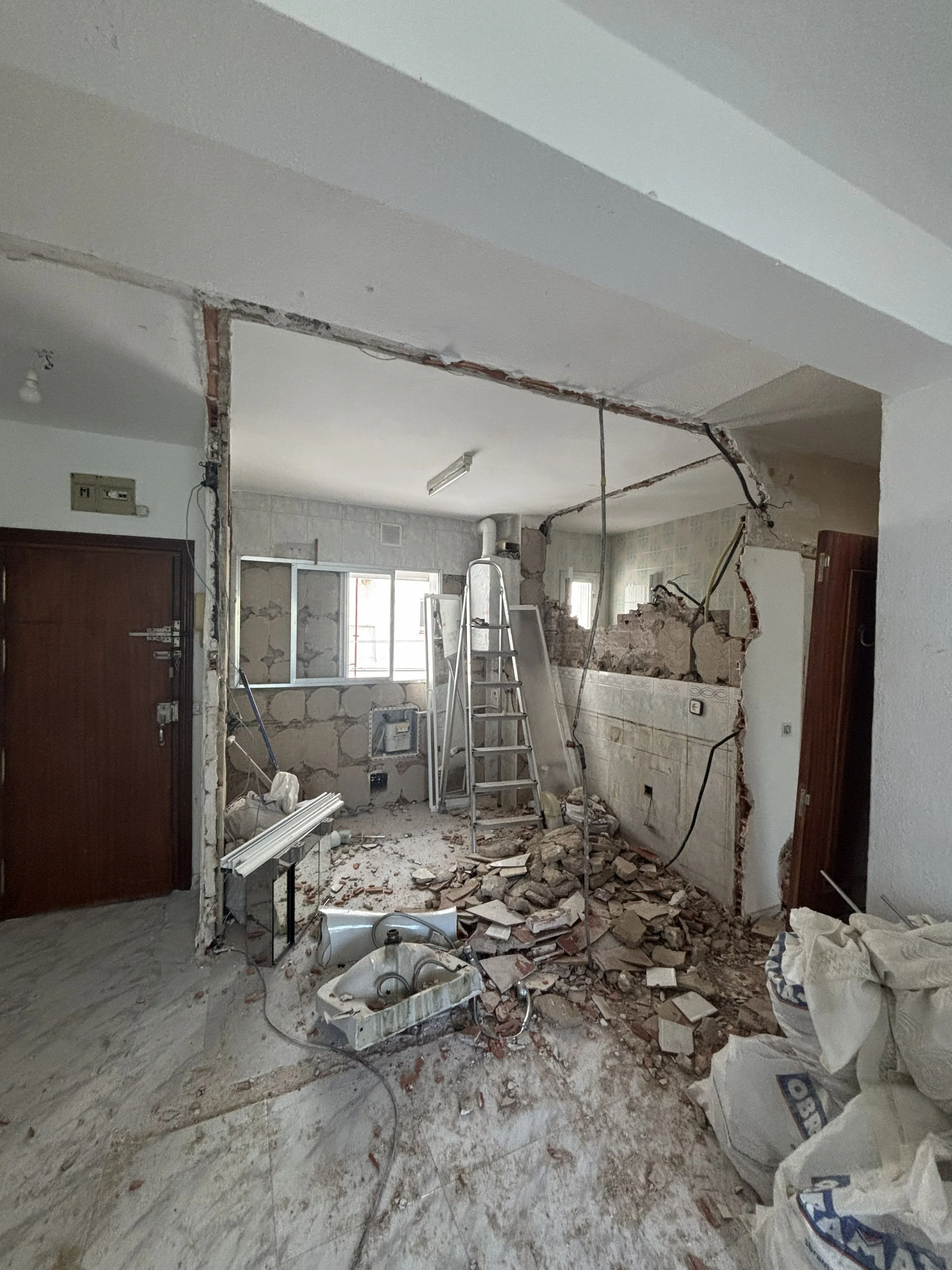 Interior en proceso de demolición con escombros y herramientas de construcción, parcialmente abierta la pared del fondo.