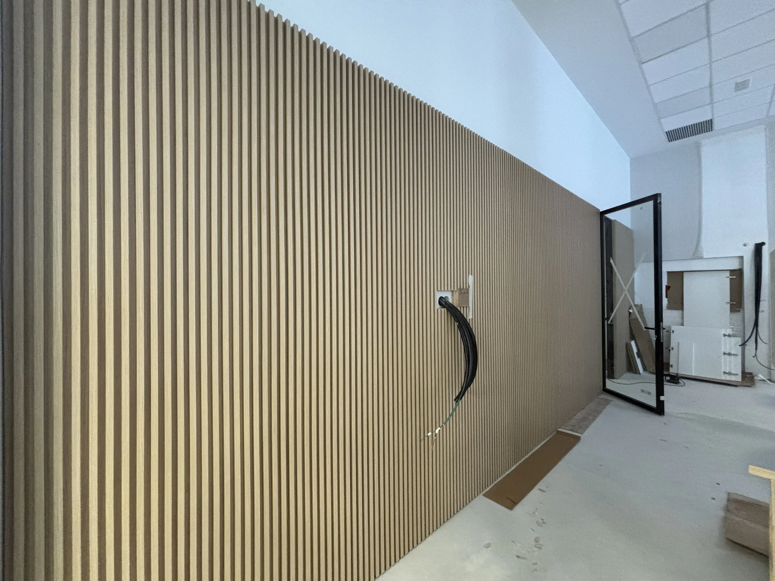 Pared de madera con ranuras verticales, en construcción, con cables y ventana abierta en una habitación moderna.