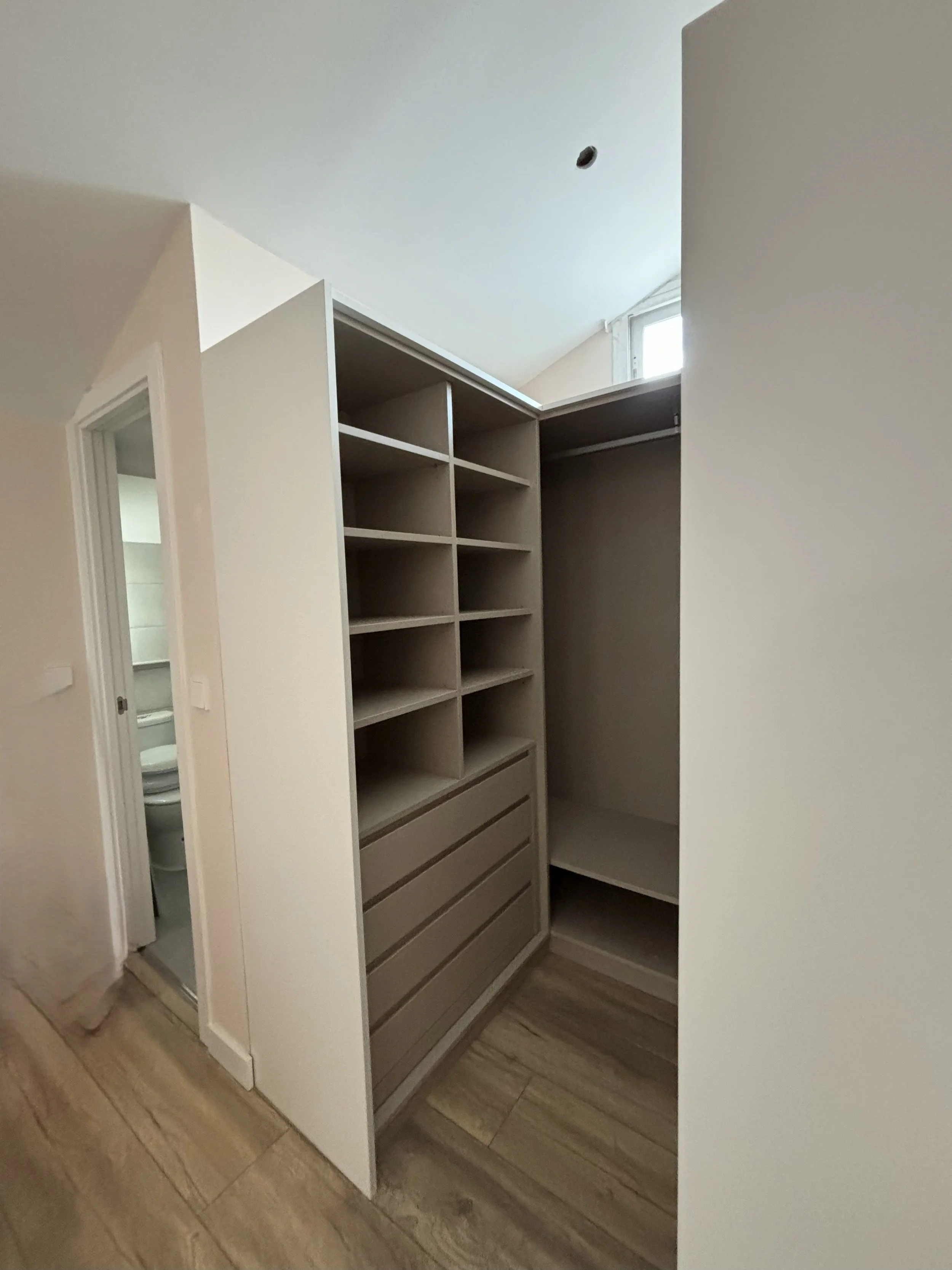 Armario empotrado con estantes, cajones y espacio para colgar ropa, en una habitación con suelo de madera.