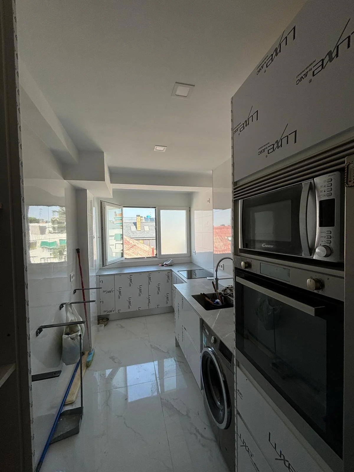 Cocina moderna en construcción, con electrodomésticos empotrados, ventanas grandes y paredes y suelo de acabado brillante.