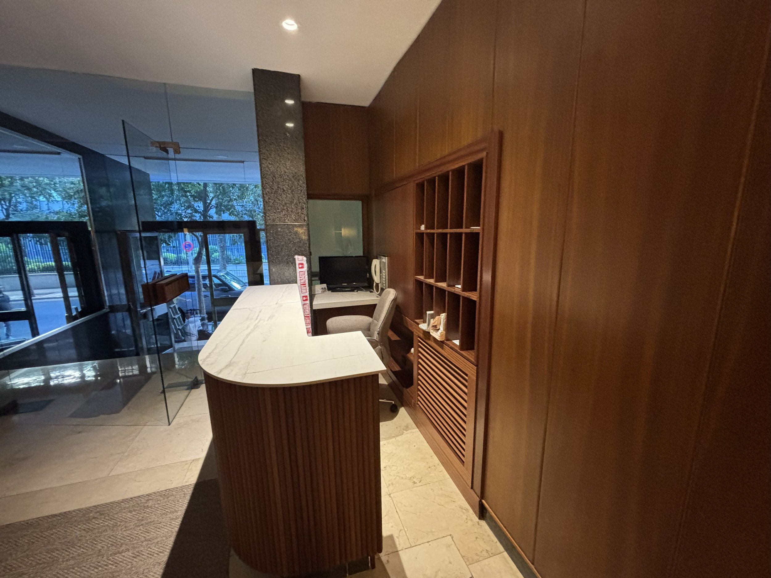 Mostrador de recepción con superficie de mármol, sillón y una estantería de madera contra la pared, en una oficina o lobby.