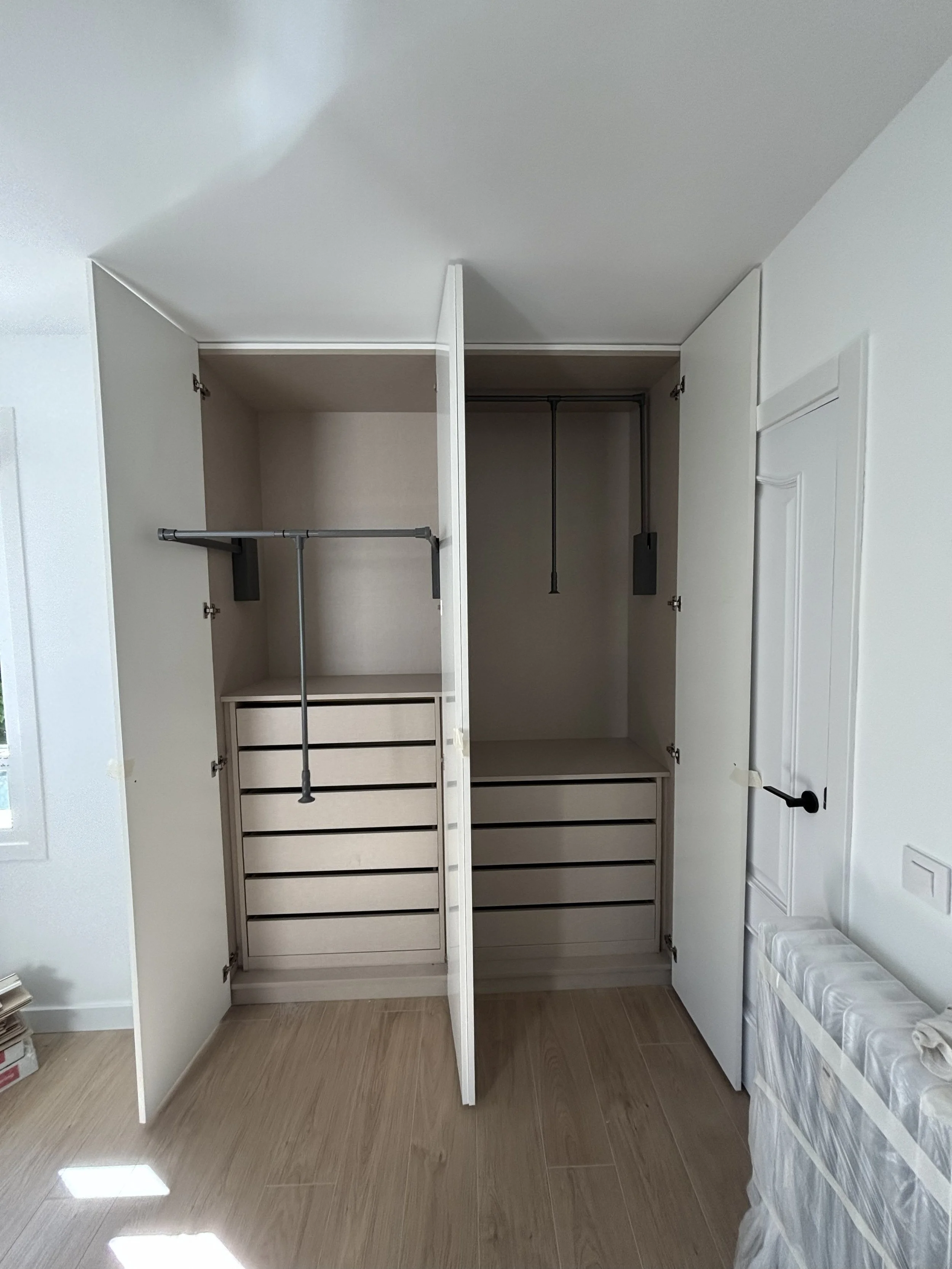 Closet abierto con varias divisiones y espacio para ropa y almacenamiento, con puertas blancas y sistema de organización.