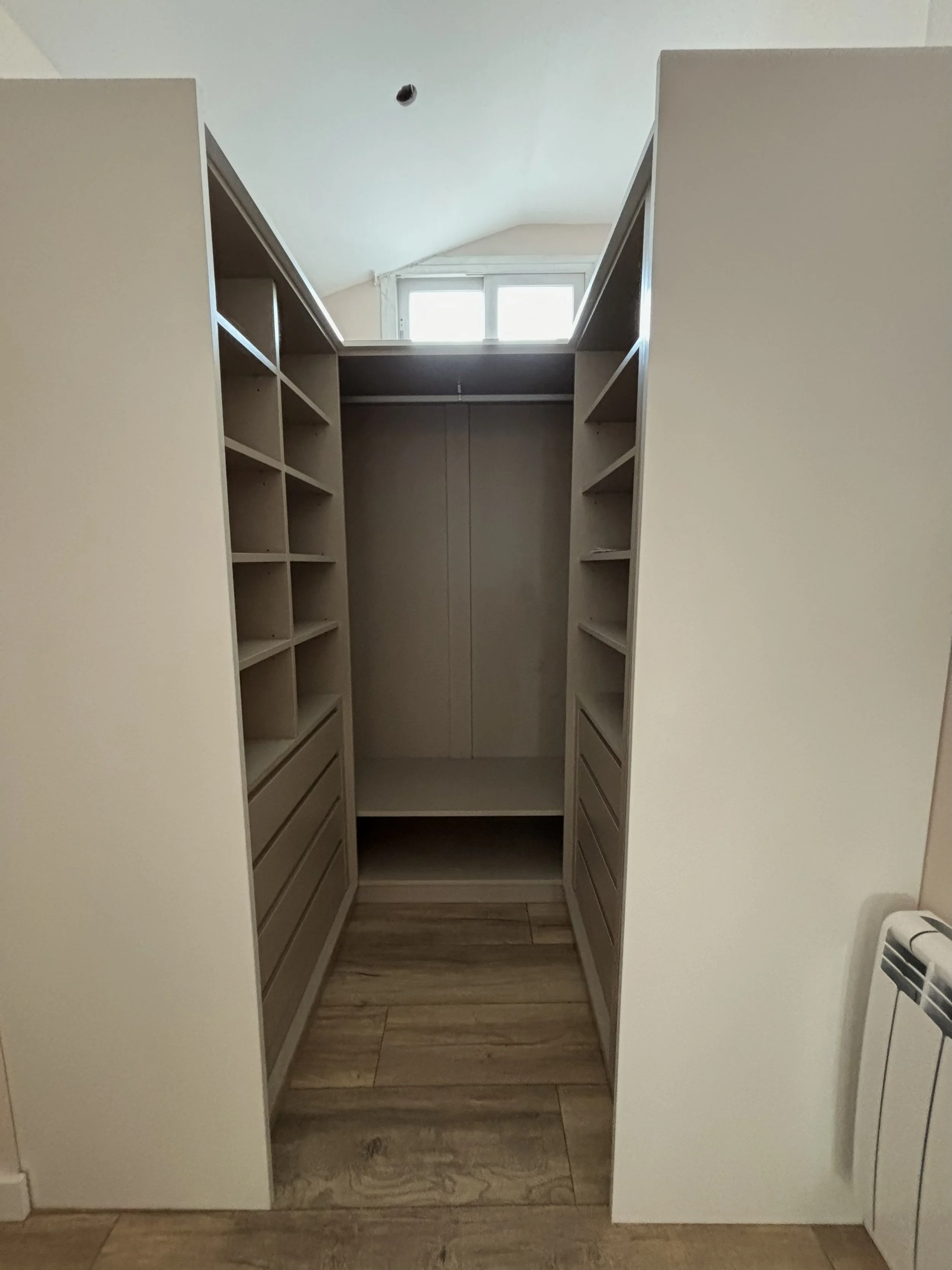 Espacio de armario vacío con estantes y cajones en un ambiente con ventana y suelo de madera.