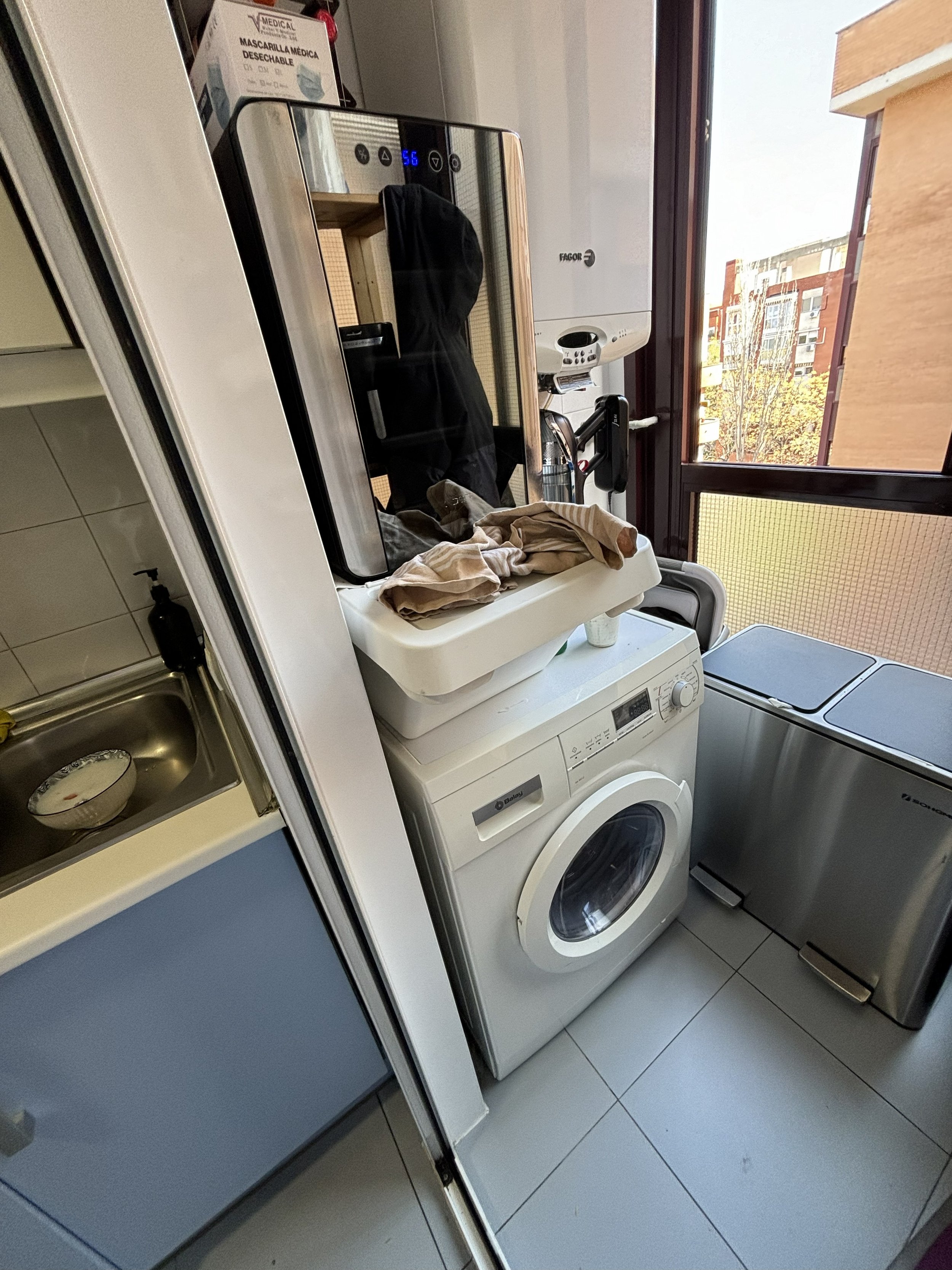 Lavadero con lavadora, secadora y armario con ventanas que muestran edificios y árboles.