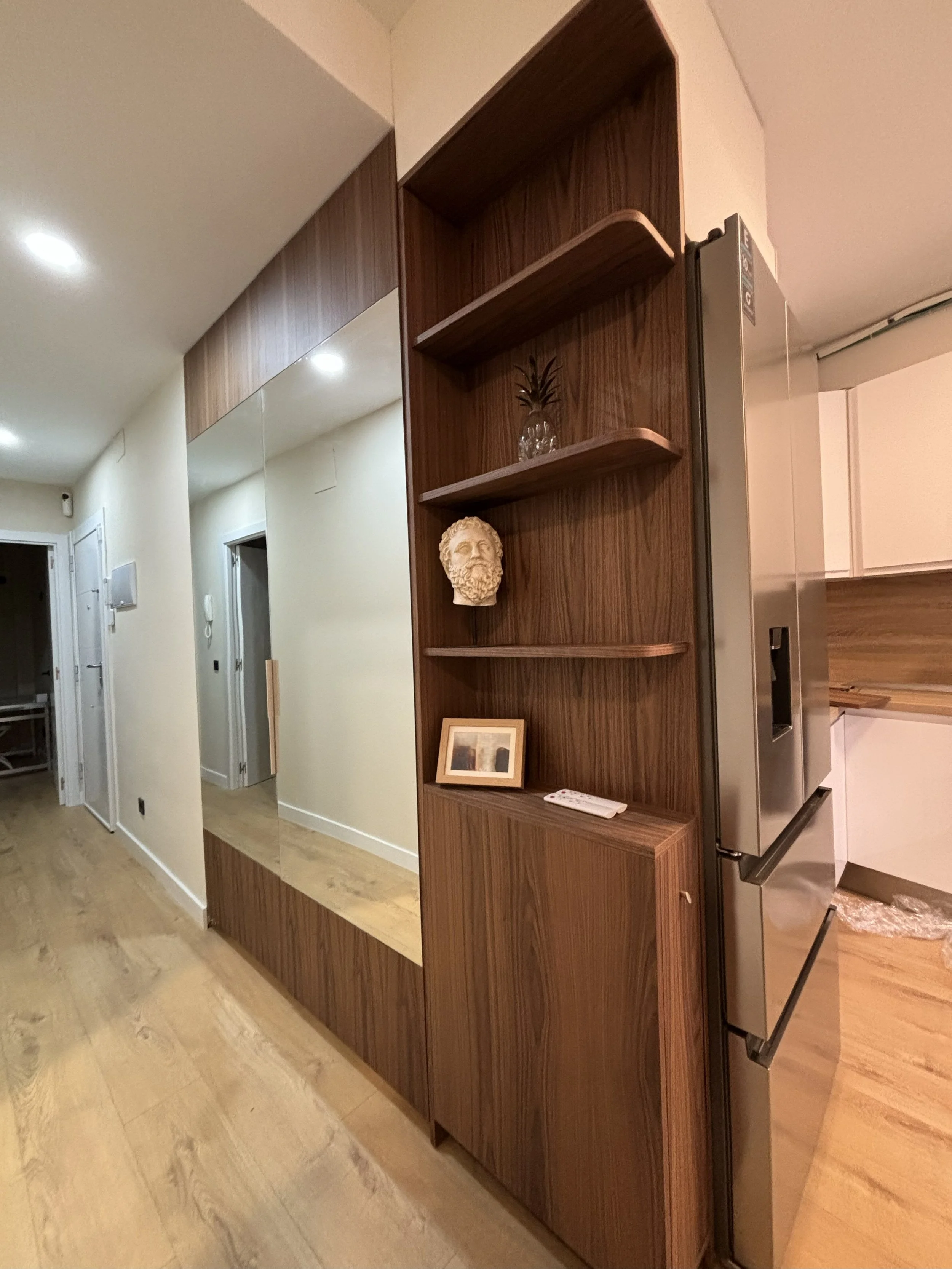 Estantería de madera en la cocina con decoraciones, incluyendo una cabeza deliciosa, una planta y un cuadro pequeño.