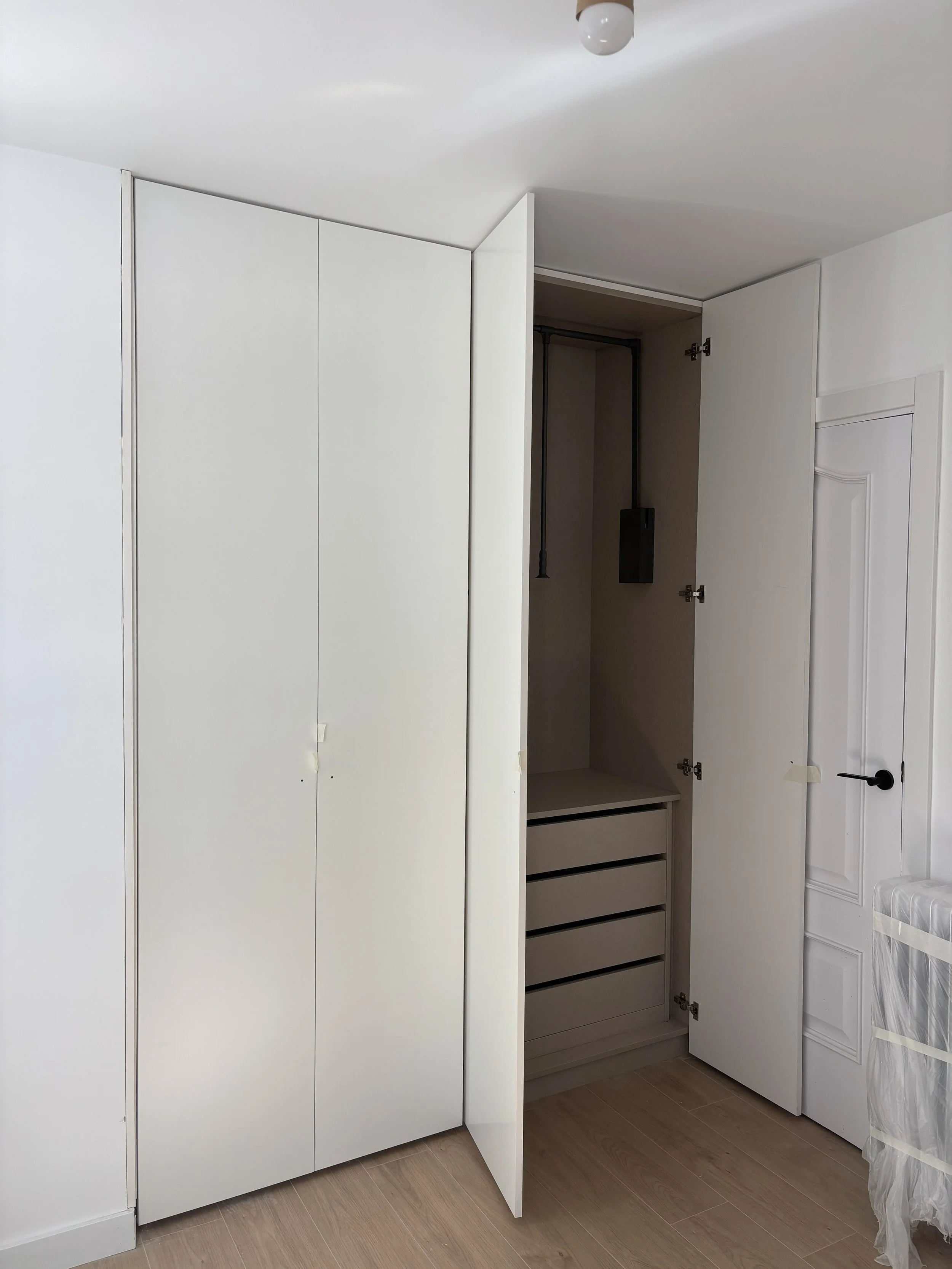 Armario blanco con puertas abiertas, mostrando espacio de almacenamiento interior con gavetas y una caja eléctrica en la parte superior.