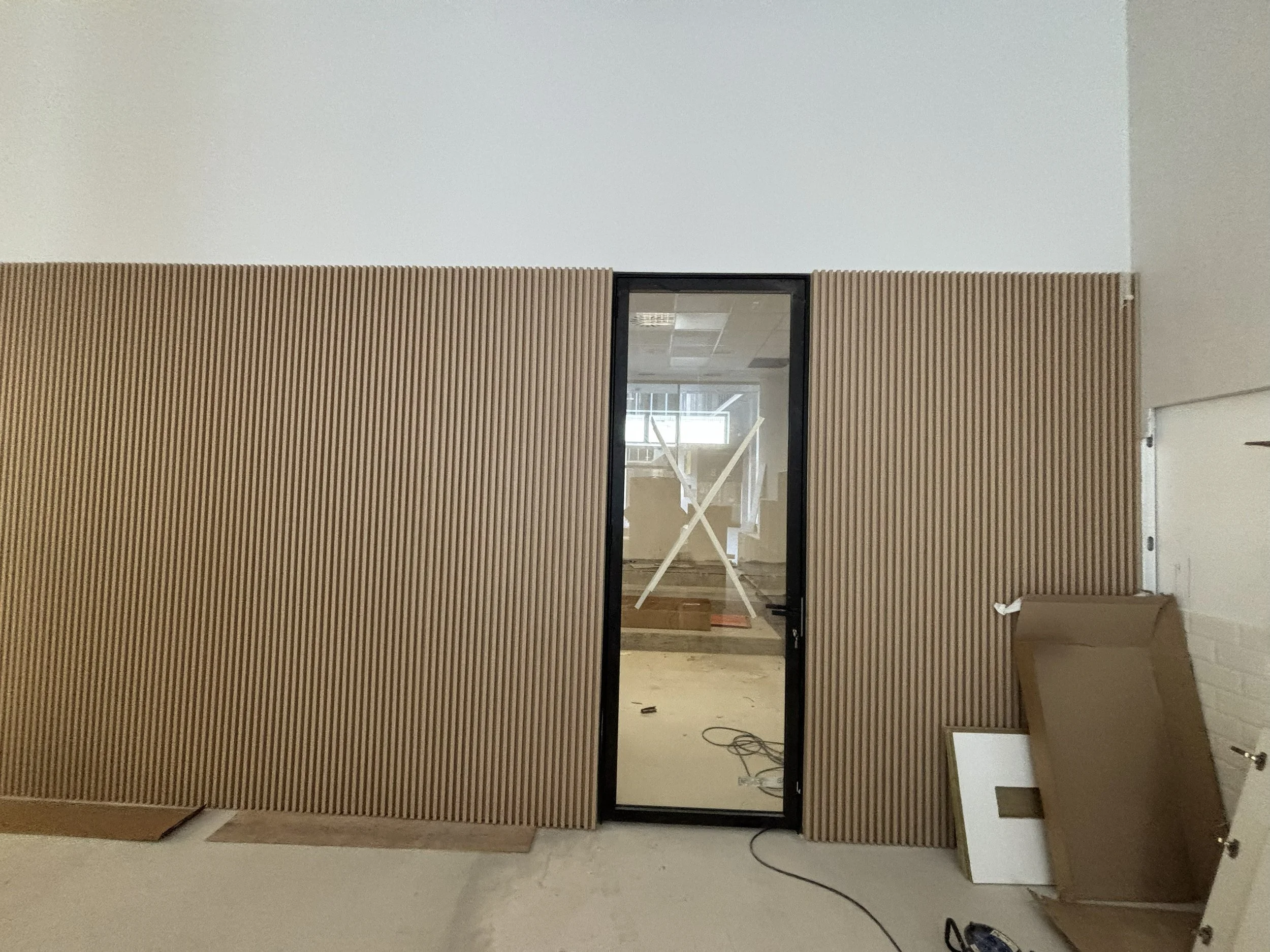 Pared de madera con puerta de cristal en una construcción interior, con materiales y herramientas en el suelo.