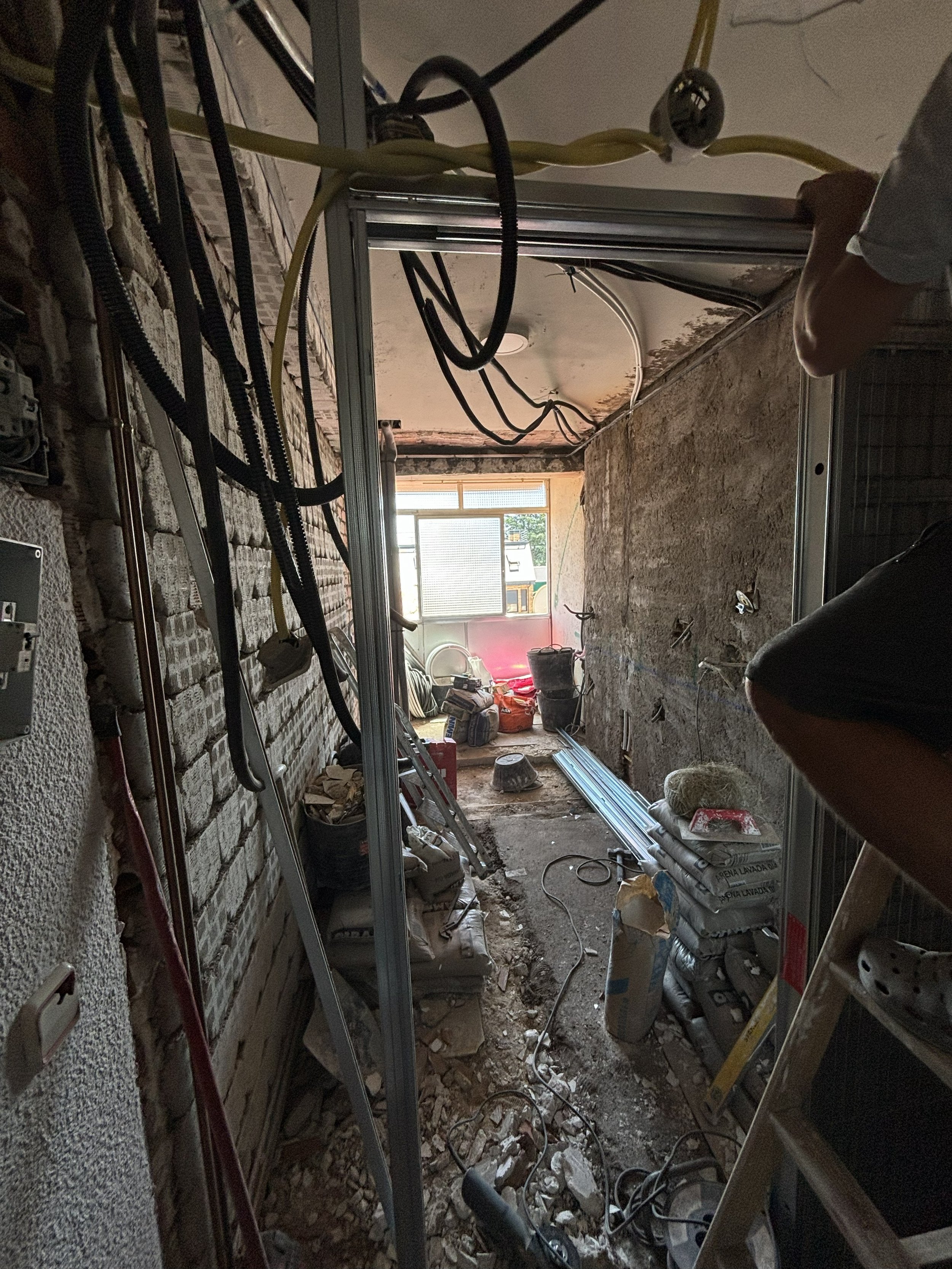 Área en construcción con cables, herramientas, bloques de piedra, y materiales de construcción, ventana al fondo