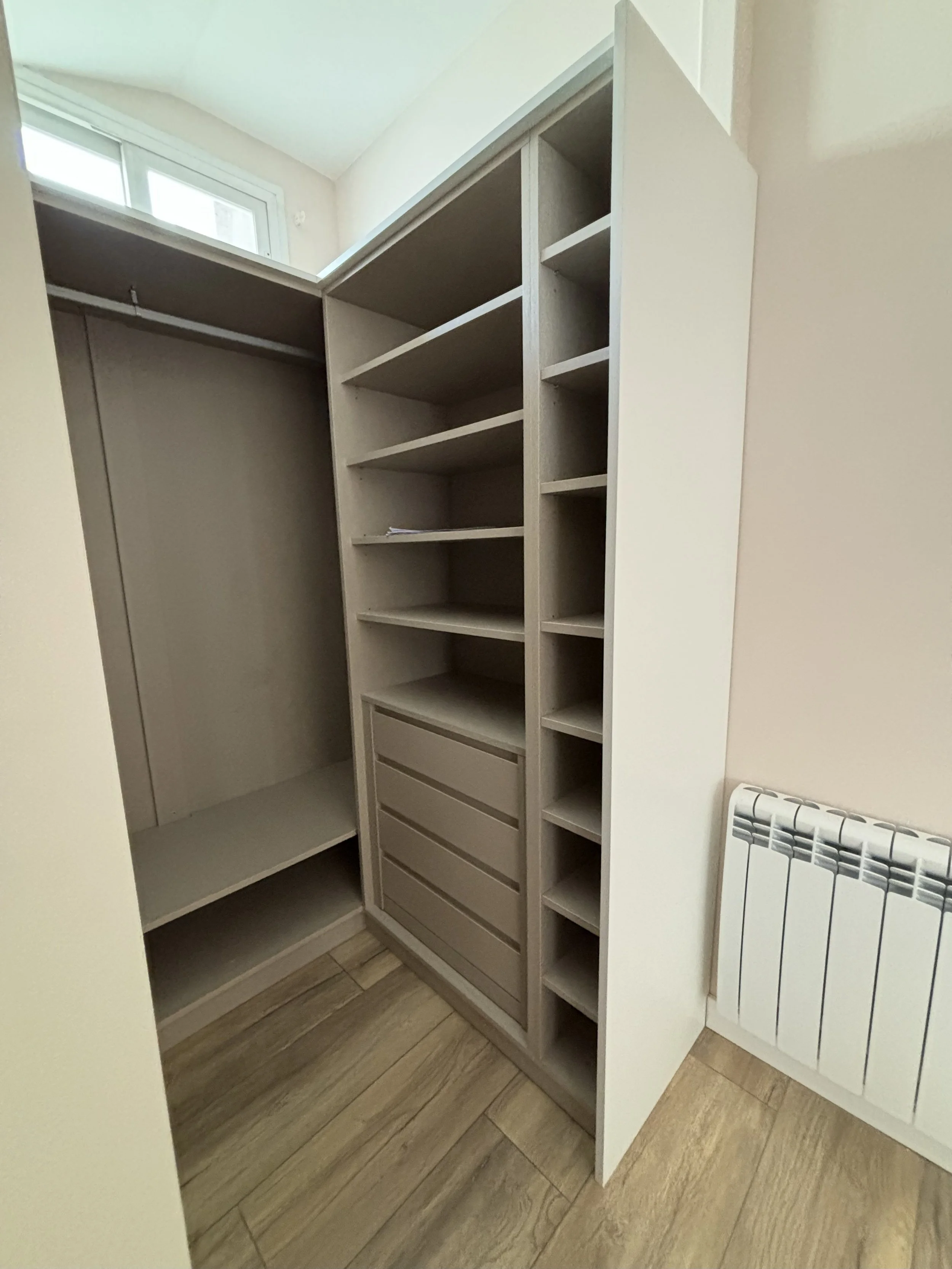 Armario con estantes y cajones en una habitación con suelo de madera y radiador en la pared.