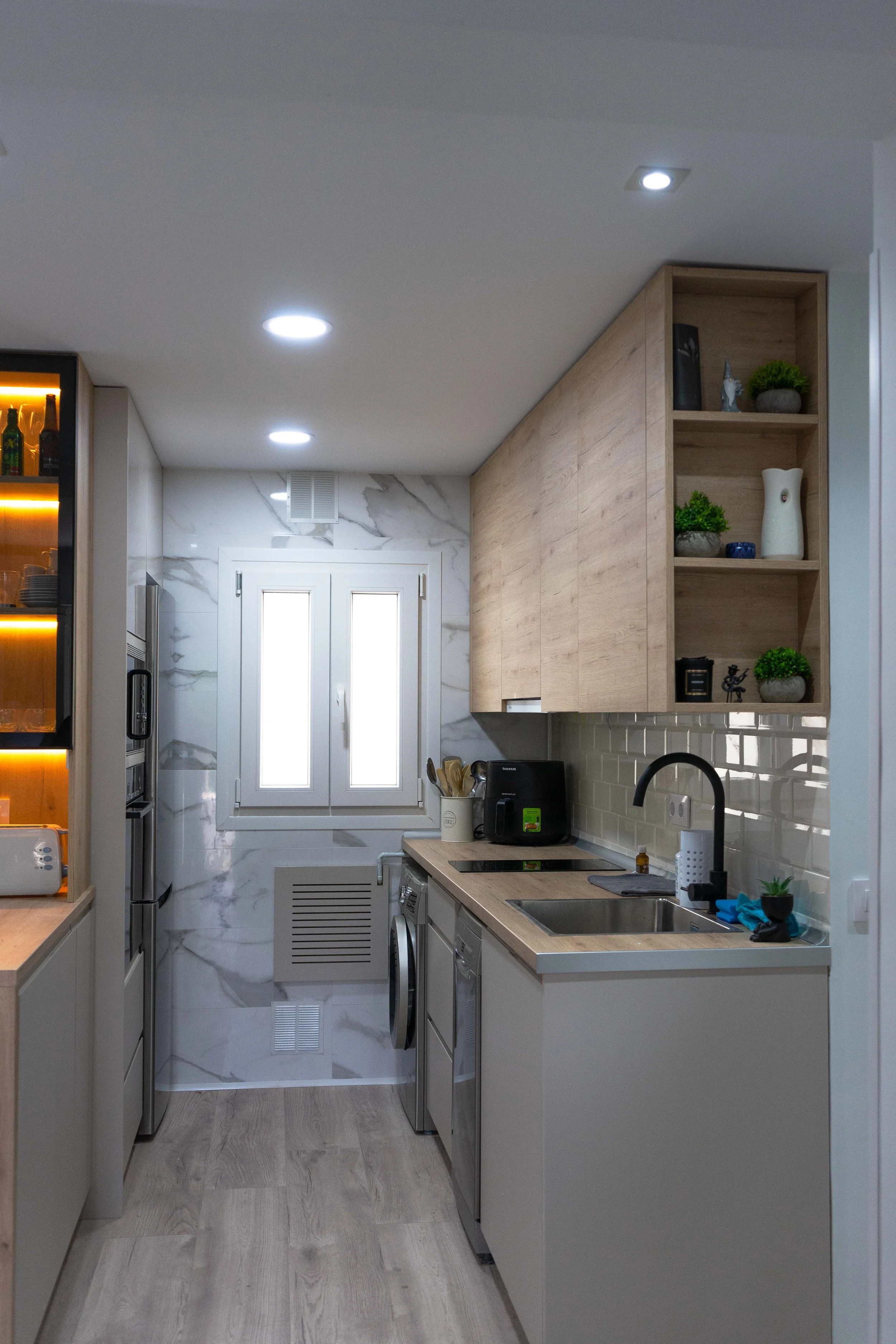 Cocina moderna con armarios de madera, electrodomésticos de acero inoxidable, estantes con decoraciones y un lavaplatos.