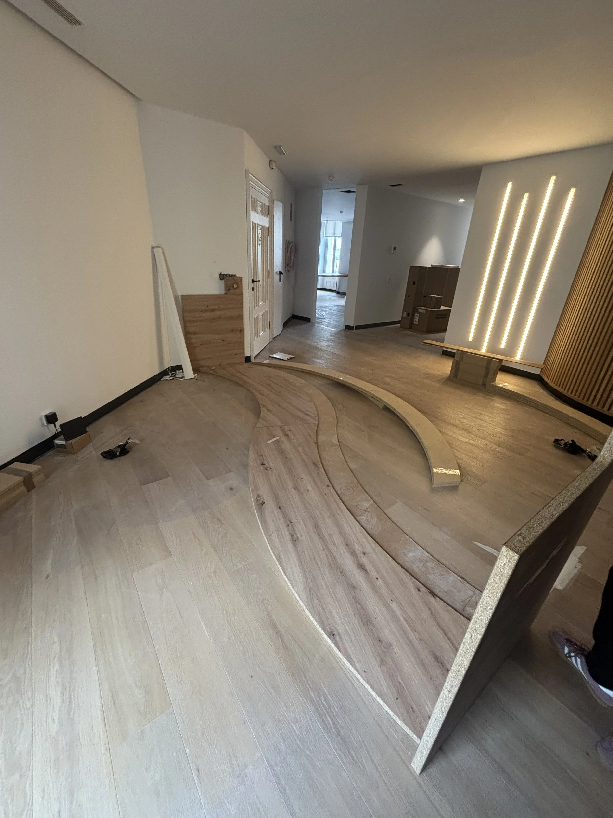 Interiores de un espacio en construcción con pisos de madera en proceso de instalación y luces empotradas en la pared.