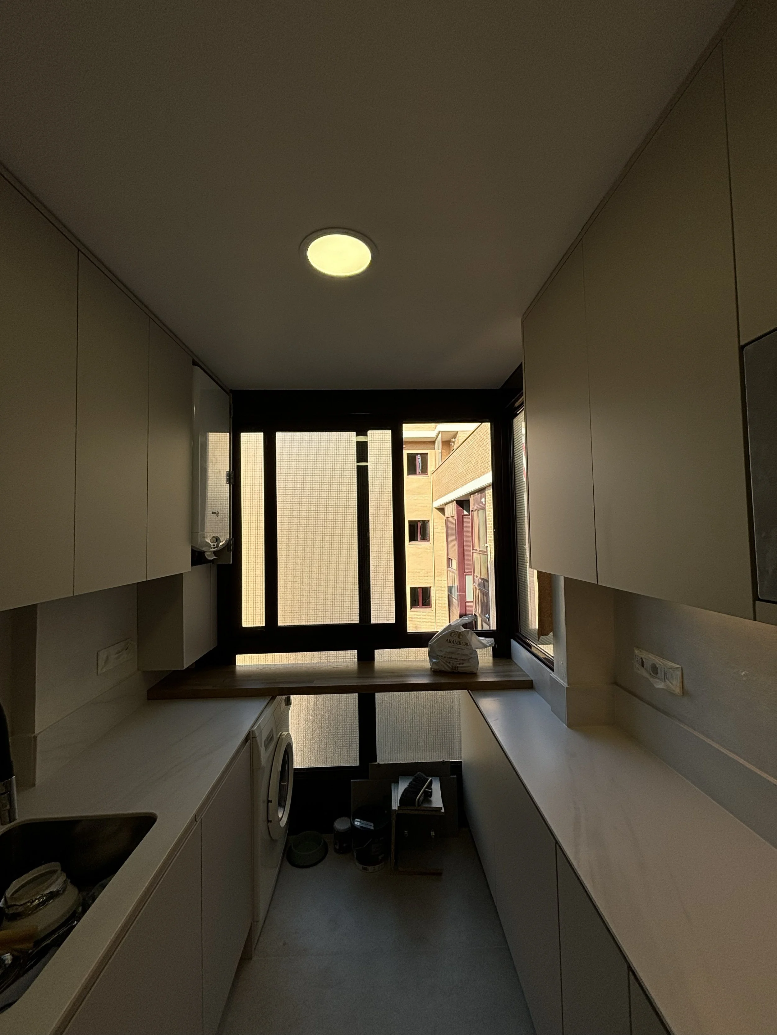 Cocina moderna con gabinetes blancos, ventana grande, y electrodomésticos, vista del edificio exterior a través de la ventana.