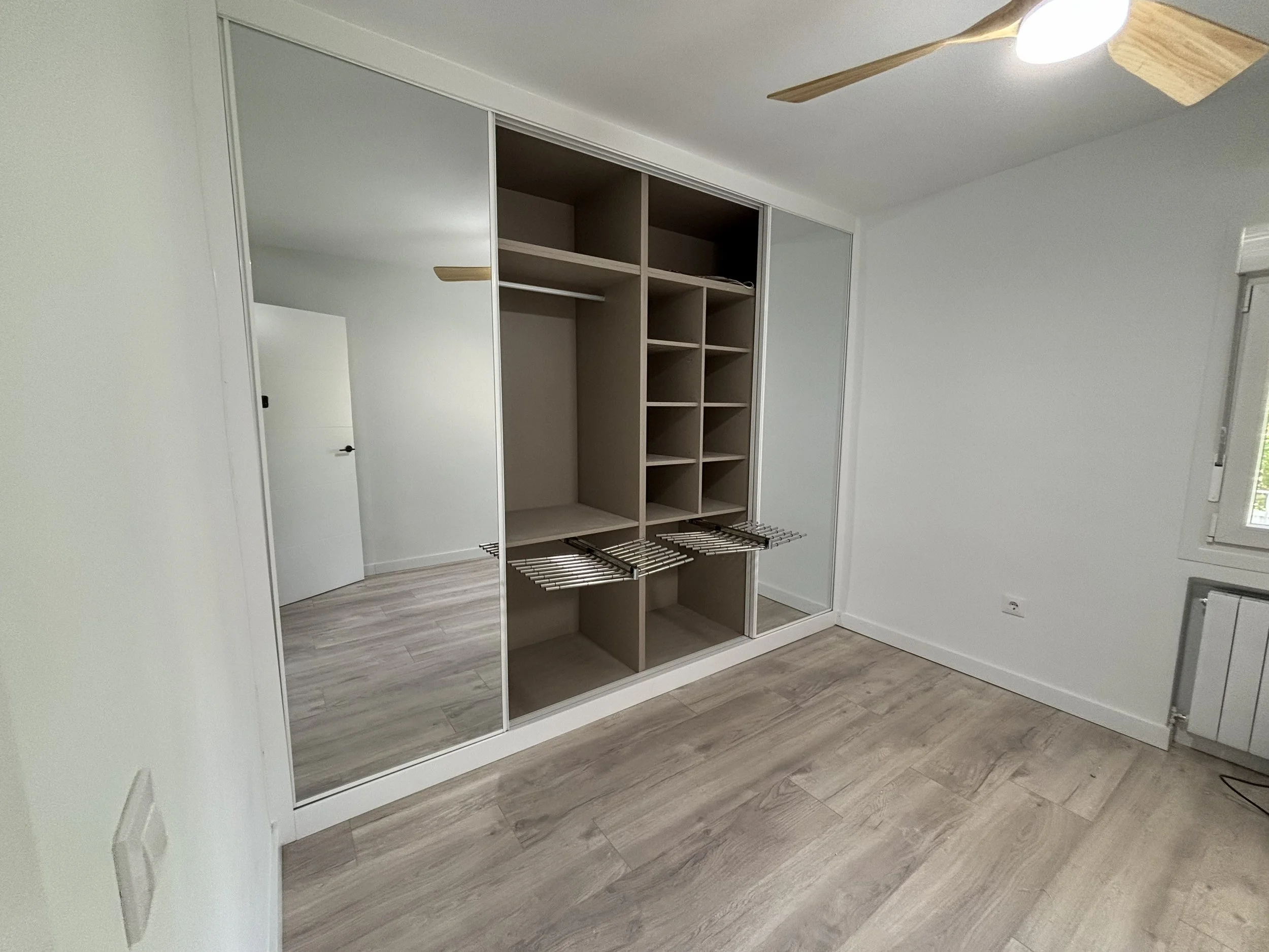 Vista de un armario de vestidor con puertas de espejo y almacenamiento abierto, y piso de madera clara.