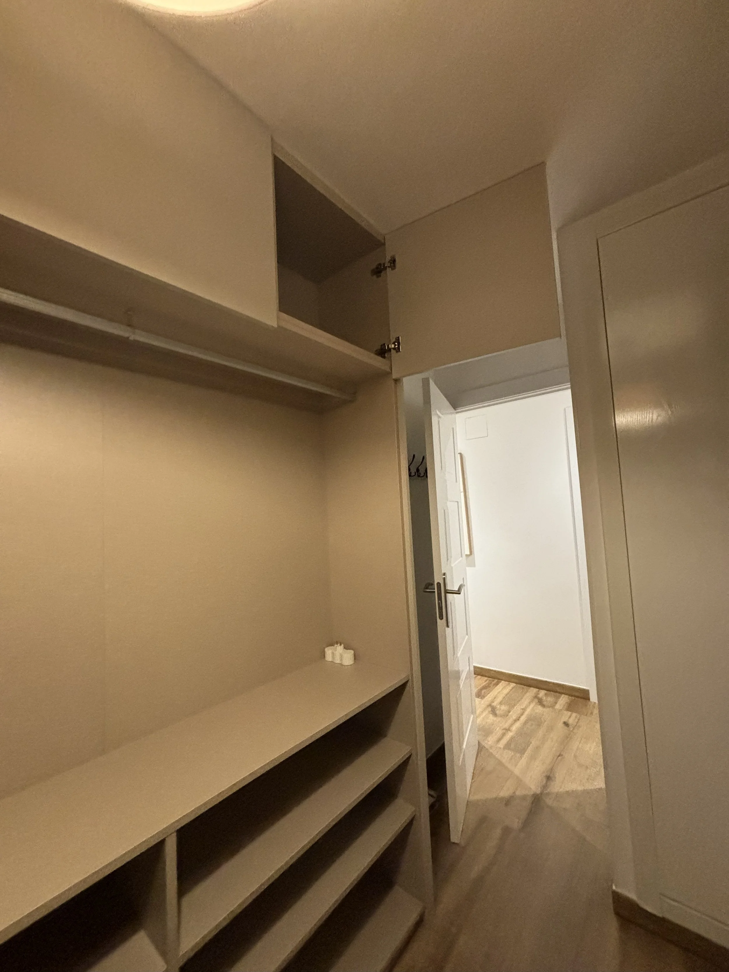 Armario de paredes blancas y estantes en un interior de casa con suelo de madera, ventanas cerradas y puerta en el fondo