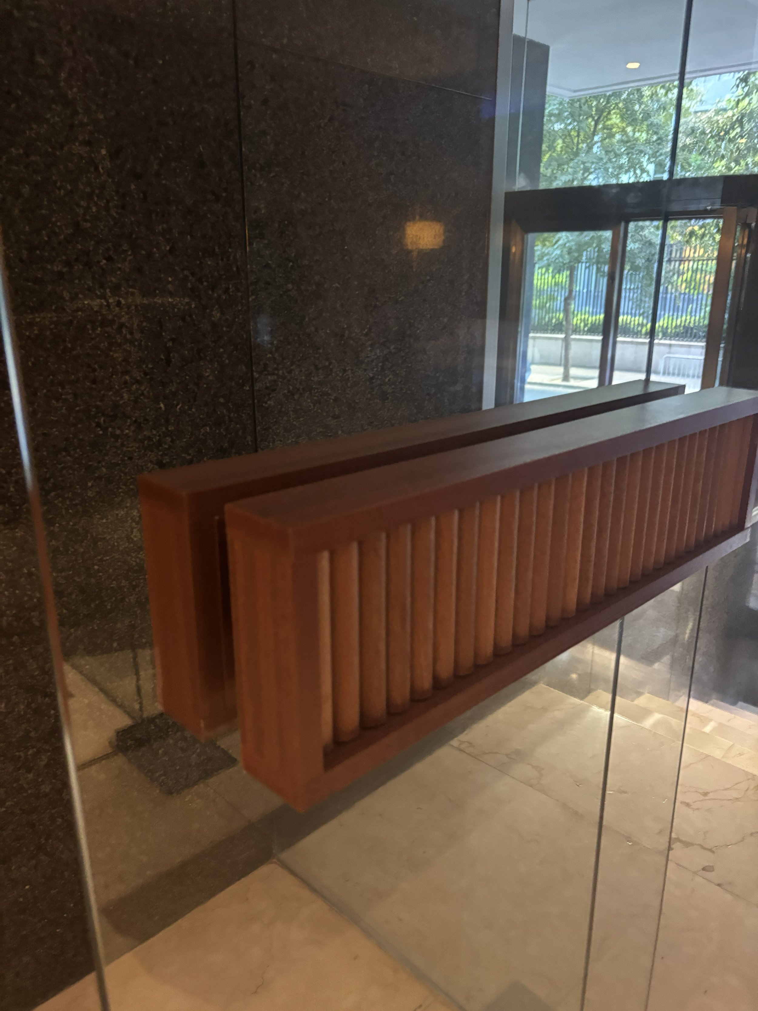 Mostrador de madera en una recepción o vestíbulo, con paredes de acabado de piedra negra y ventanas de vidrio que dejan ver árboles y luz natural.