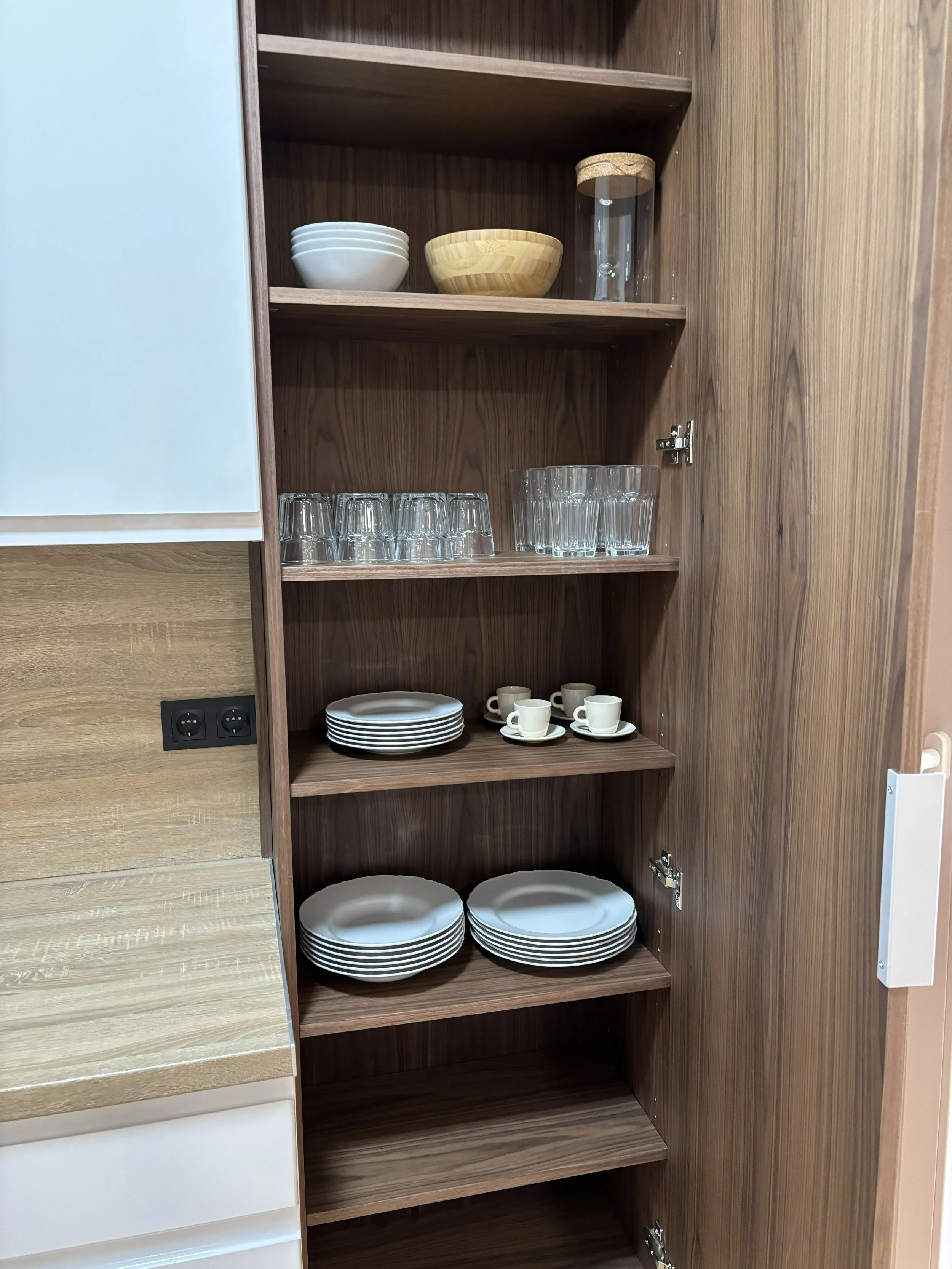 Estantería de madera con platos, tazas, vasos, cuencos y un recipiente con tapadera.