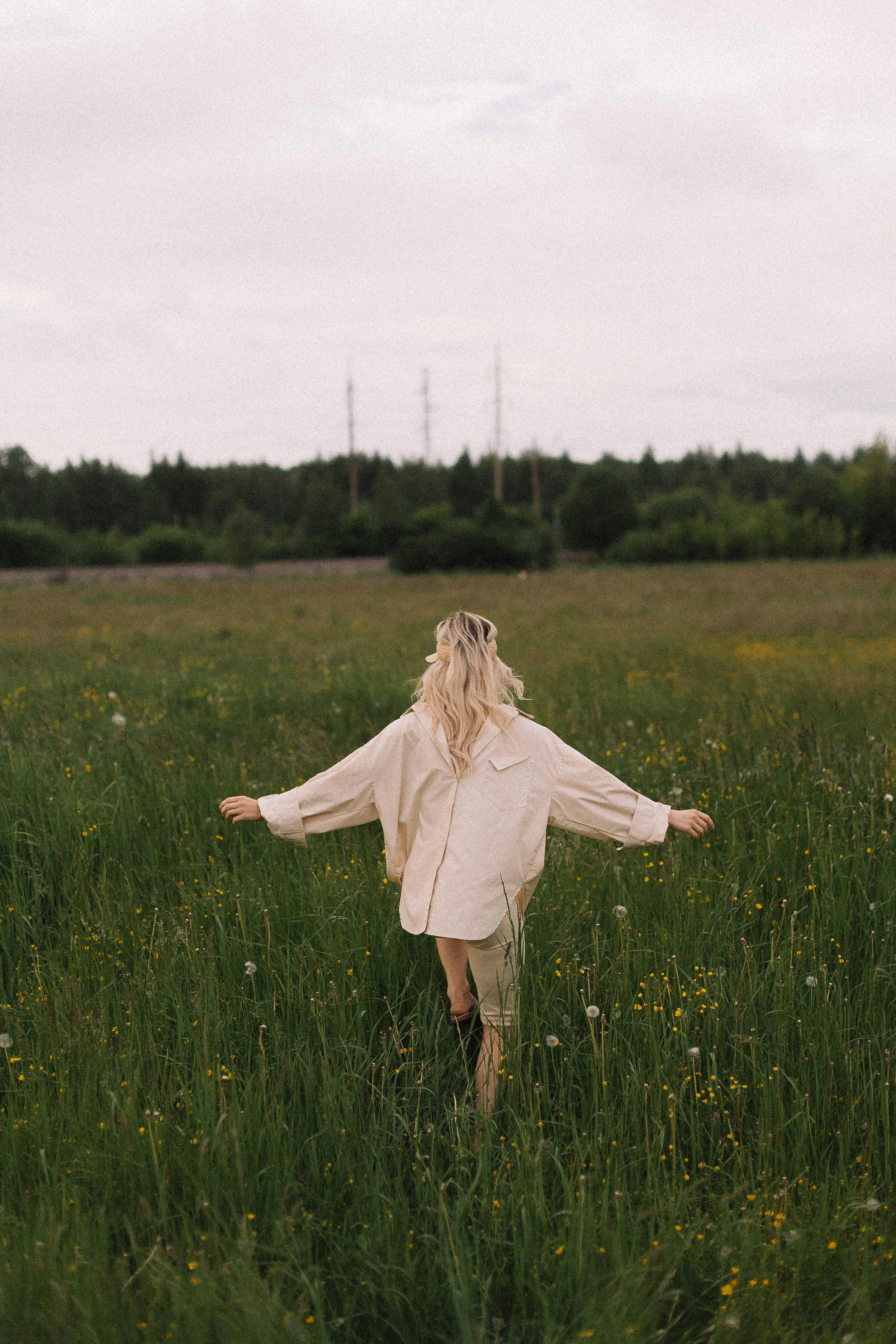 An image depicting a woman in a beige coat walking barefoot through a grassy field representing therapy for women and therapy for college students specializing in Therapy for Narcissistic Abuse in East Lansing, MI.