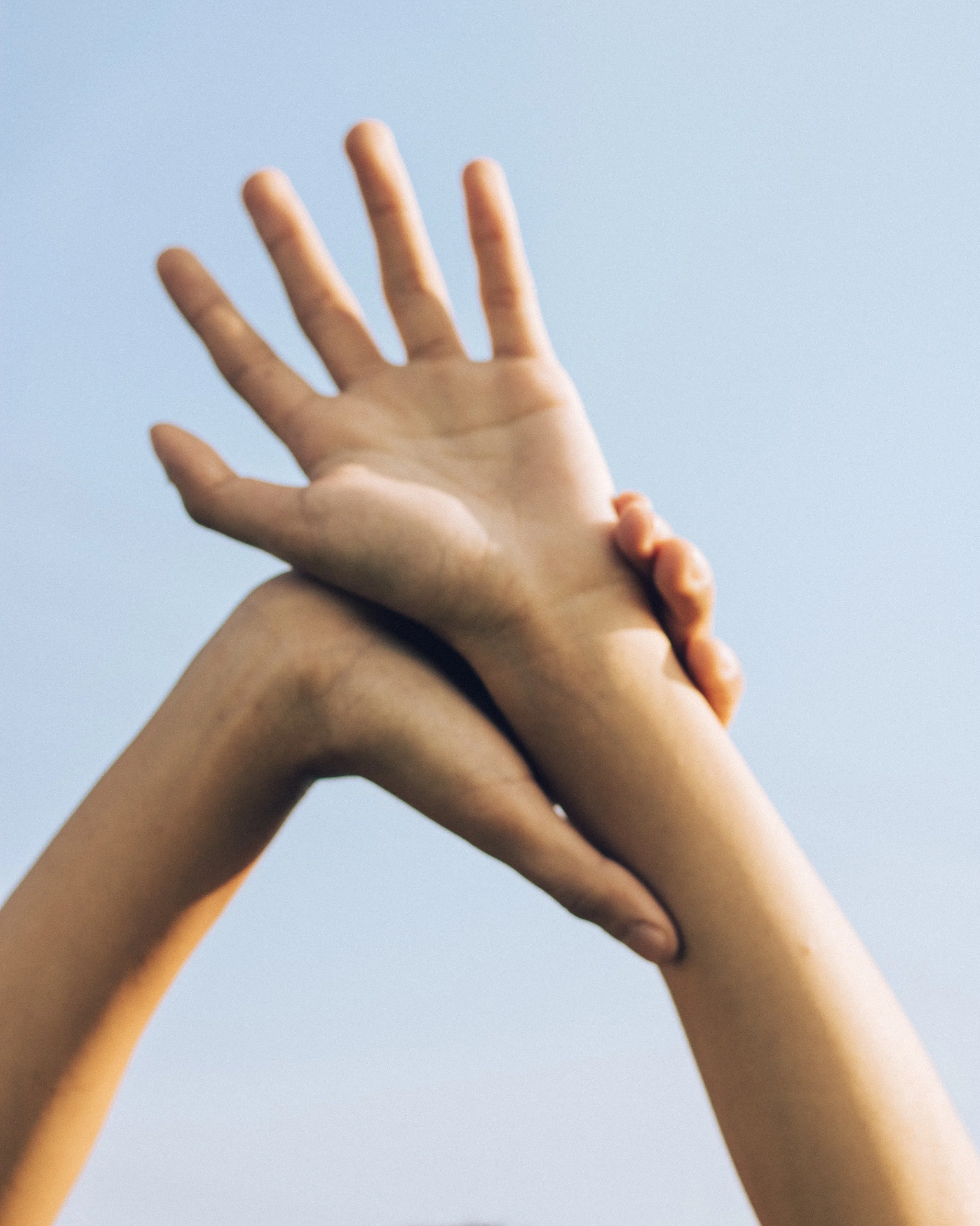 Hands stretching in a restorative yoga posture in front of a bright, blue sky