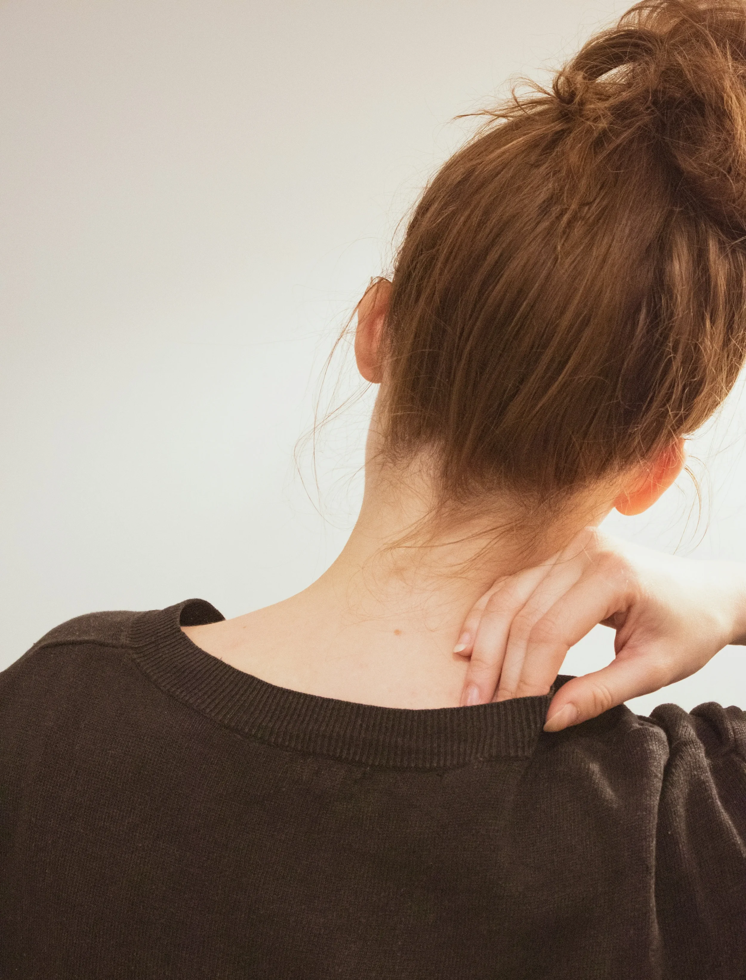 Person gently touching the back of their neck, representing body awareness used in eating disorder therapy in Los Angeles