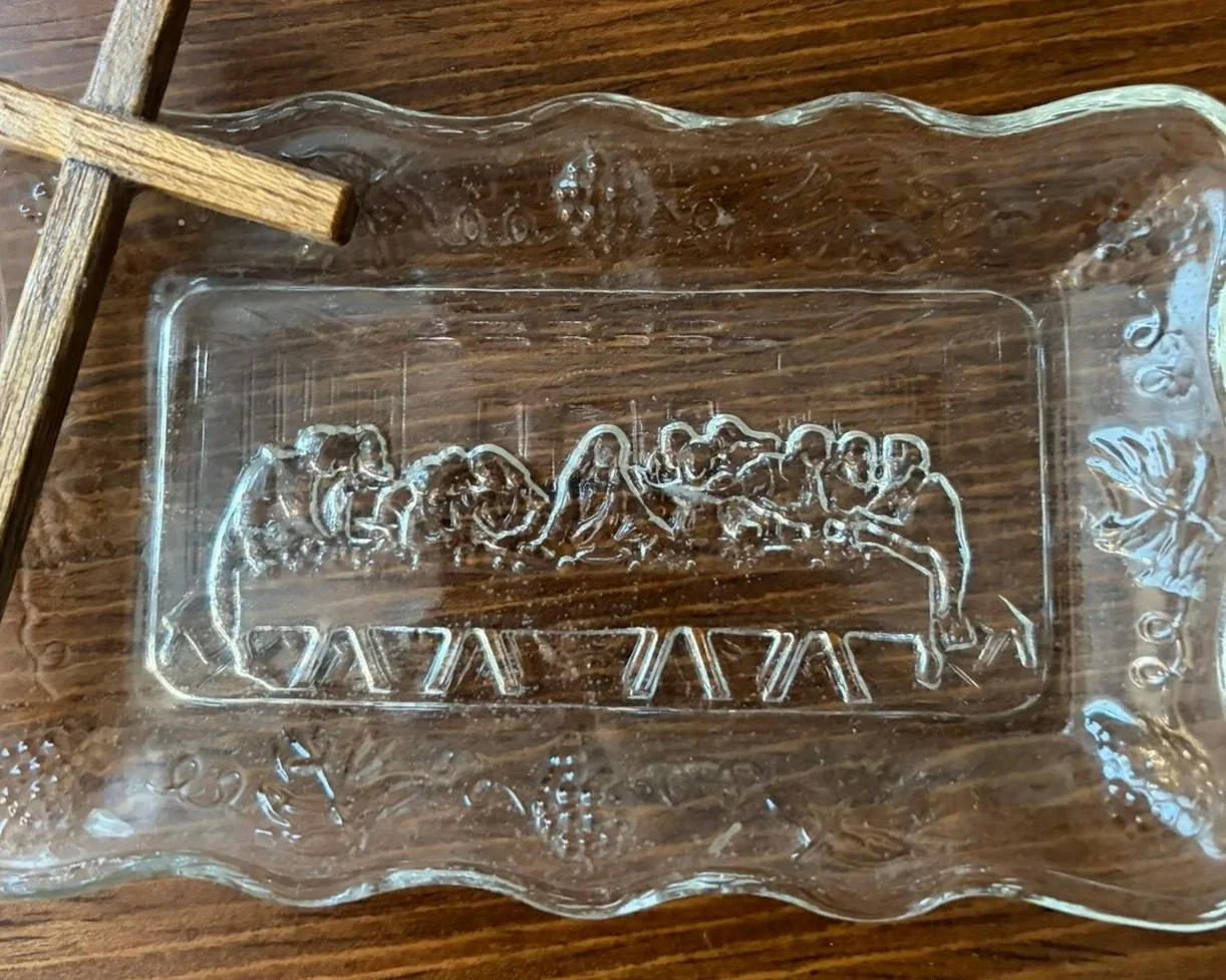 A clear glass dish featuring a detailed engraving of The Last Supper from the Bible, placed on a wooden surface.