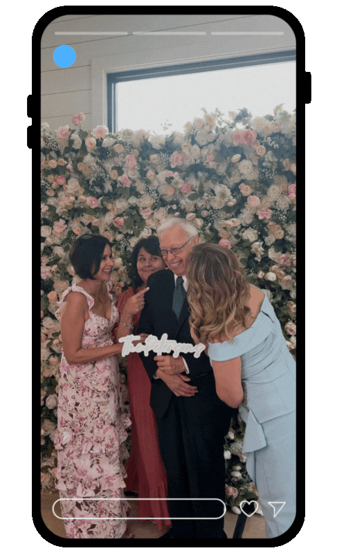 People celebrating a wedding or special event with a floral backdrop and a 'Today' sign, including a woman in a floral dress, a man in a suit with glasses, and two women touching or hugging.