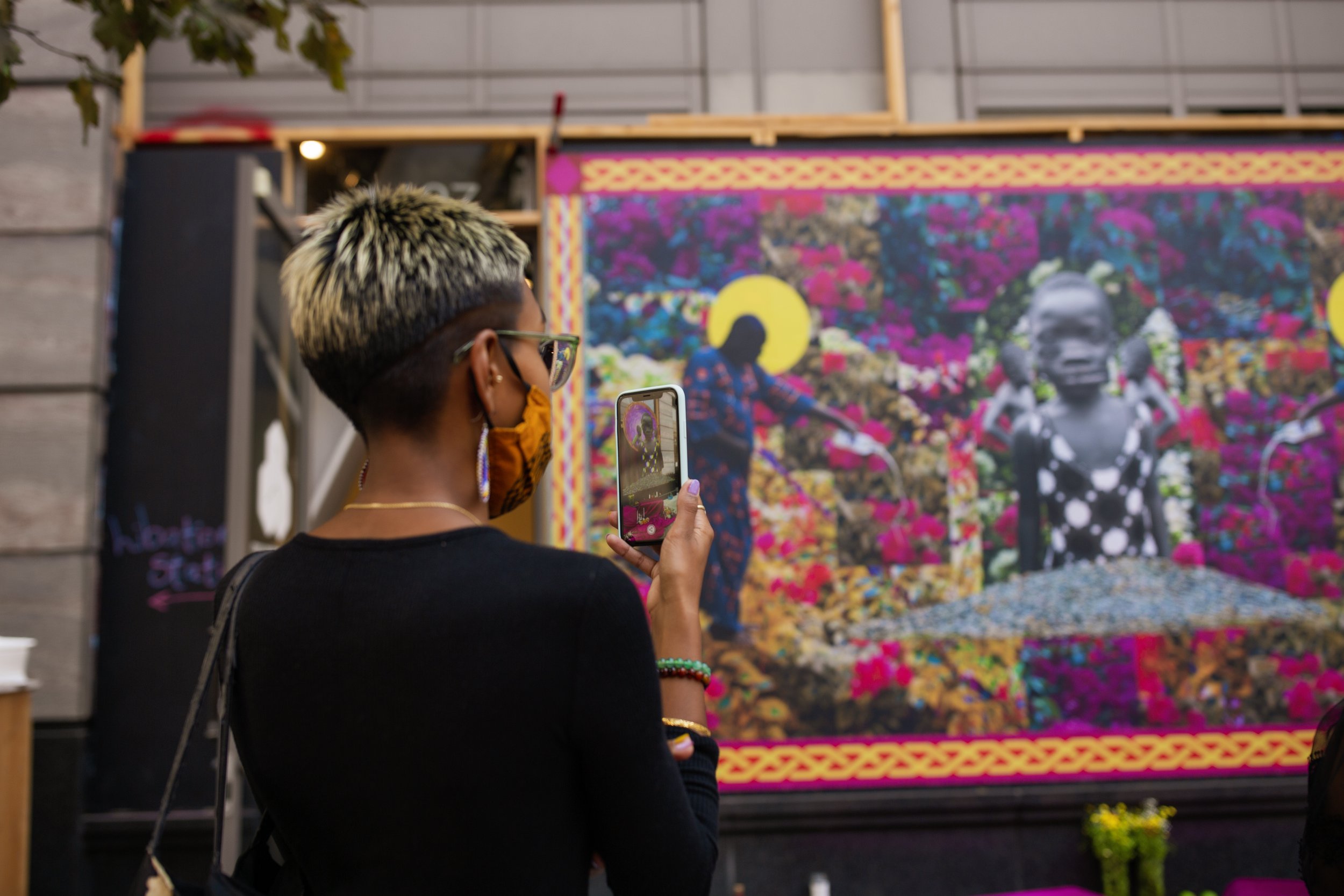  Someone wearing a face mask and holding a smartphone, taking a photo of an art installation 