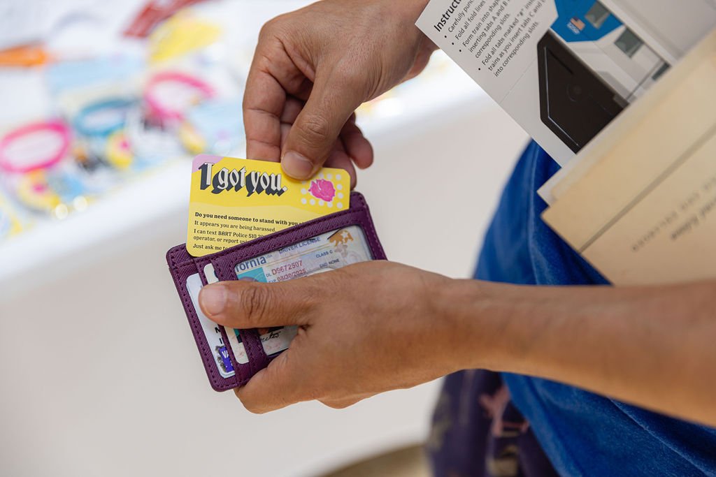  Hands holding a wallet sized card of the Our Story of Courage campaign being placed in a brown wallet 