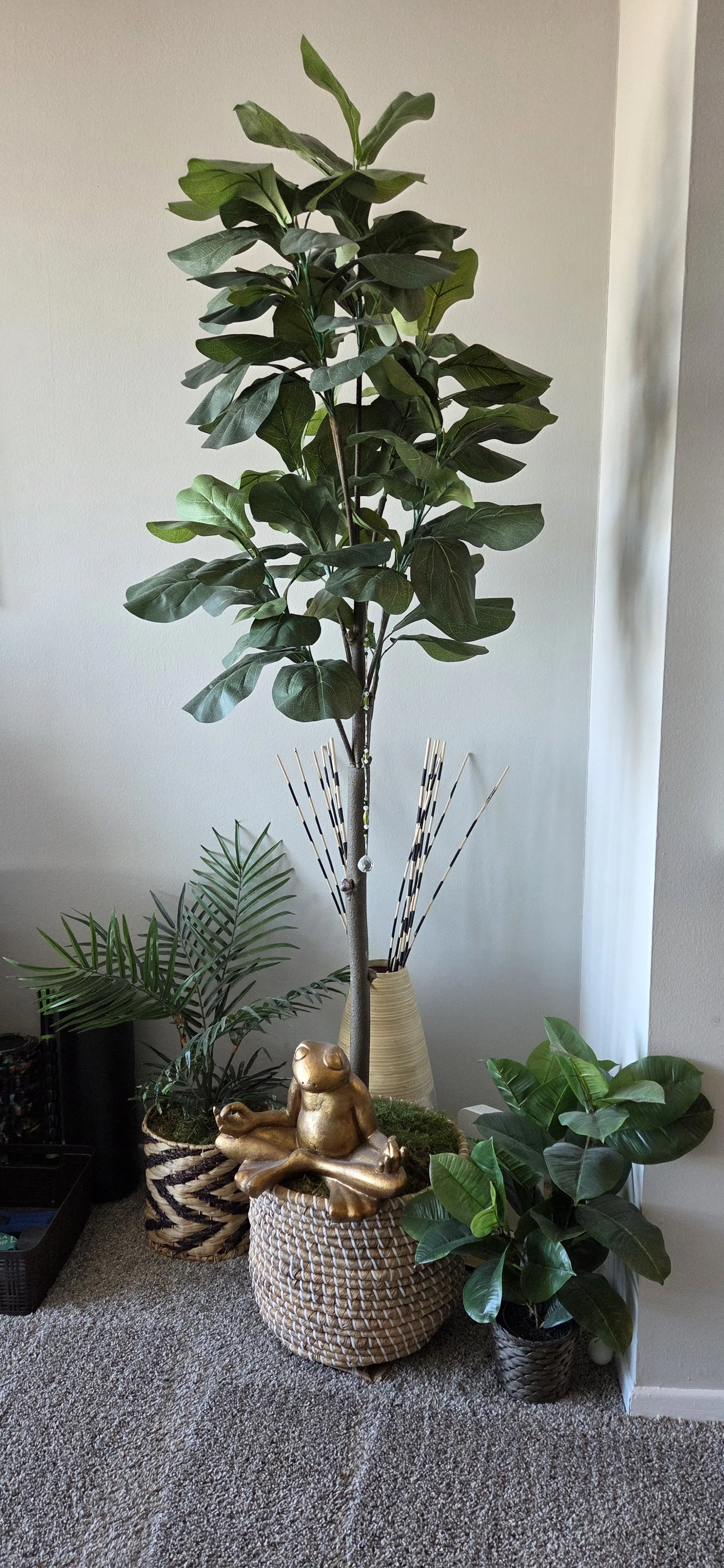 An image of plants in a corner of a room with a gold meditating frog