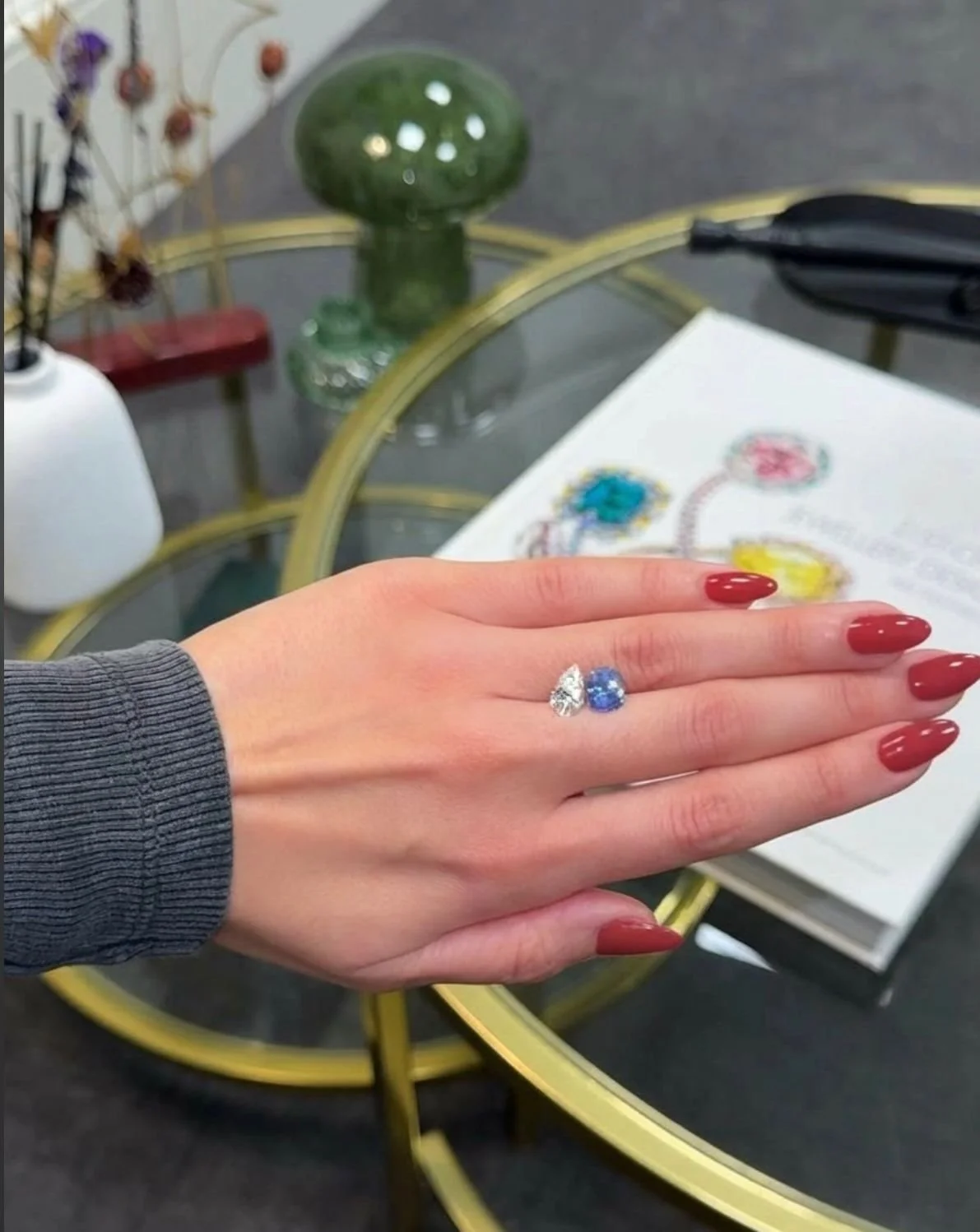 A woman showing off a sparkling heart-shaped diamond ring and a blue gemstone ring on her finger.