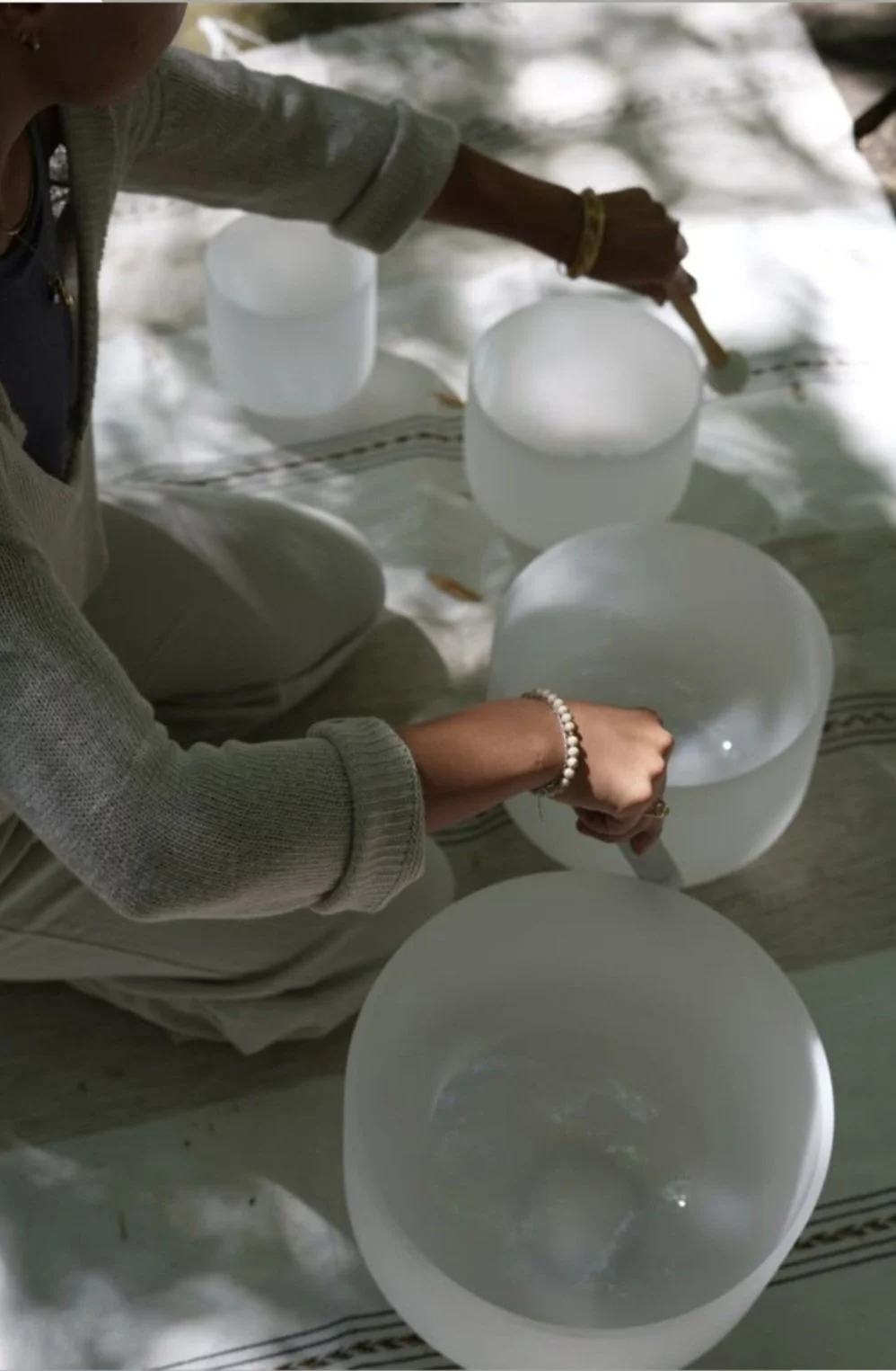 Person playing crystal singing bowls on a striped cloth.