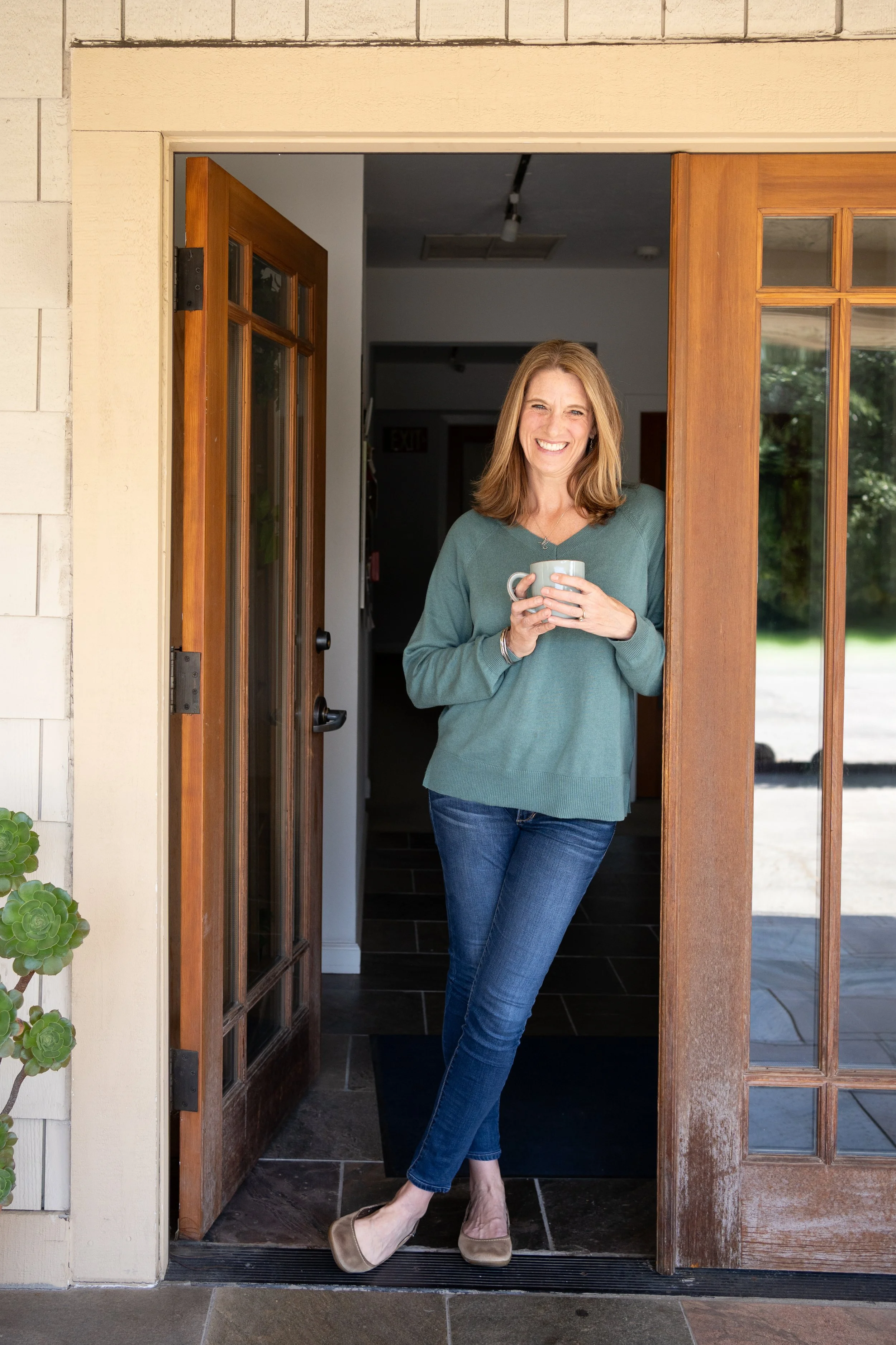 Reagan Glover, LMFT, a trauma-informed therapist in California, smiling in the doorway of her therapy office in Scotts Valley
