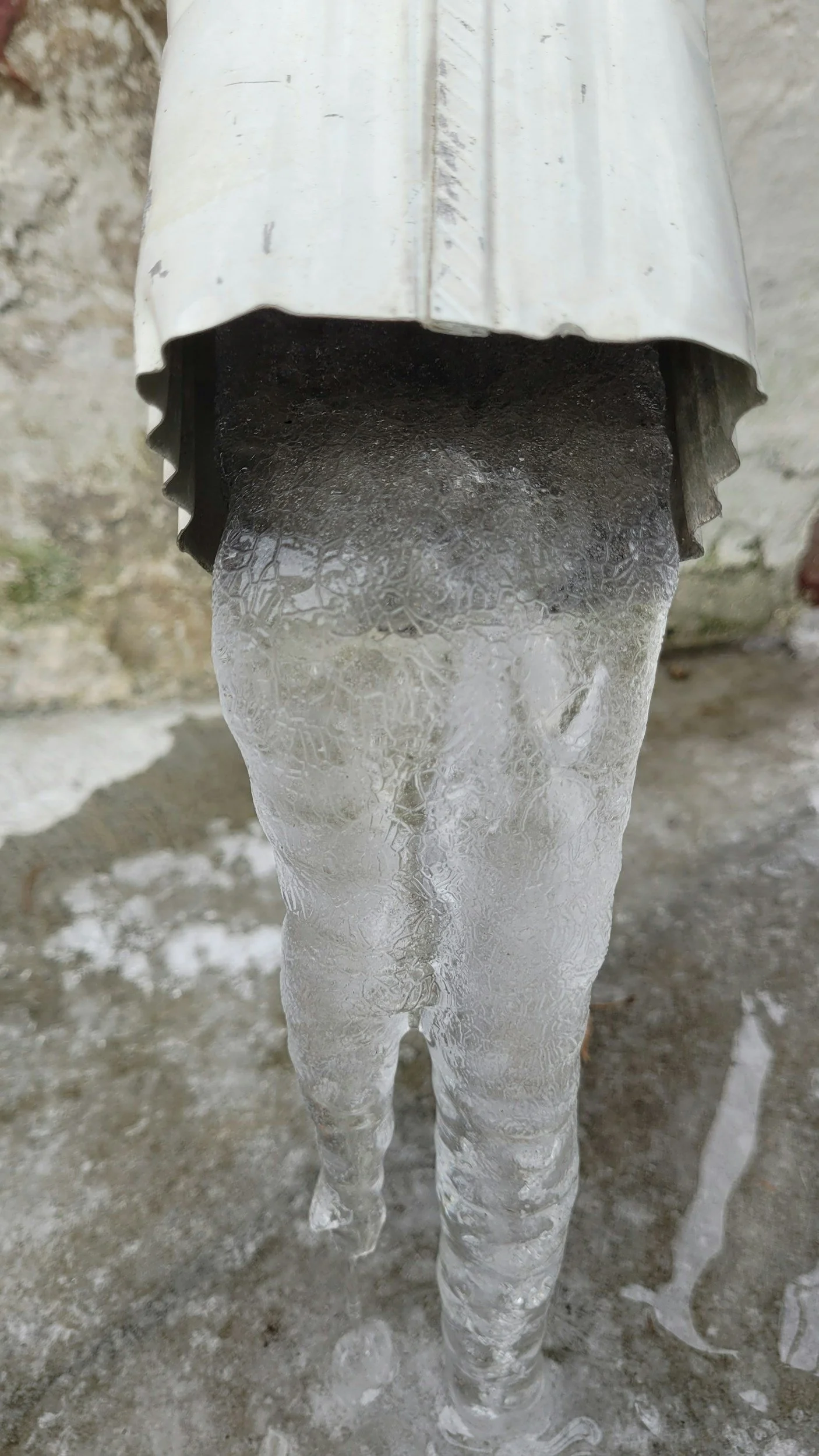 An outdoor fire hydrant with a metal cap, releasing a column of ice formed from water freezing in the cold weather.
