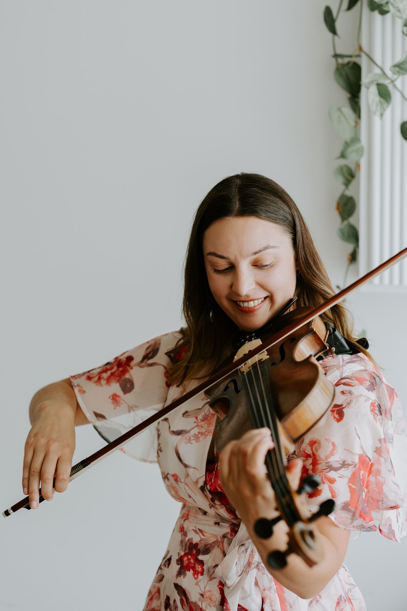 A woman with brown hair wearing a floral dress playing the violin.